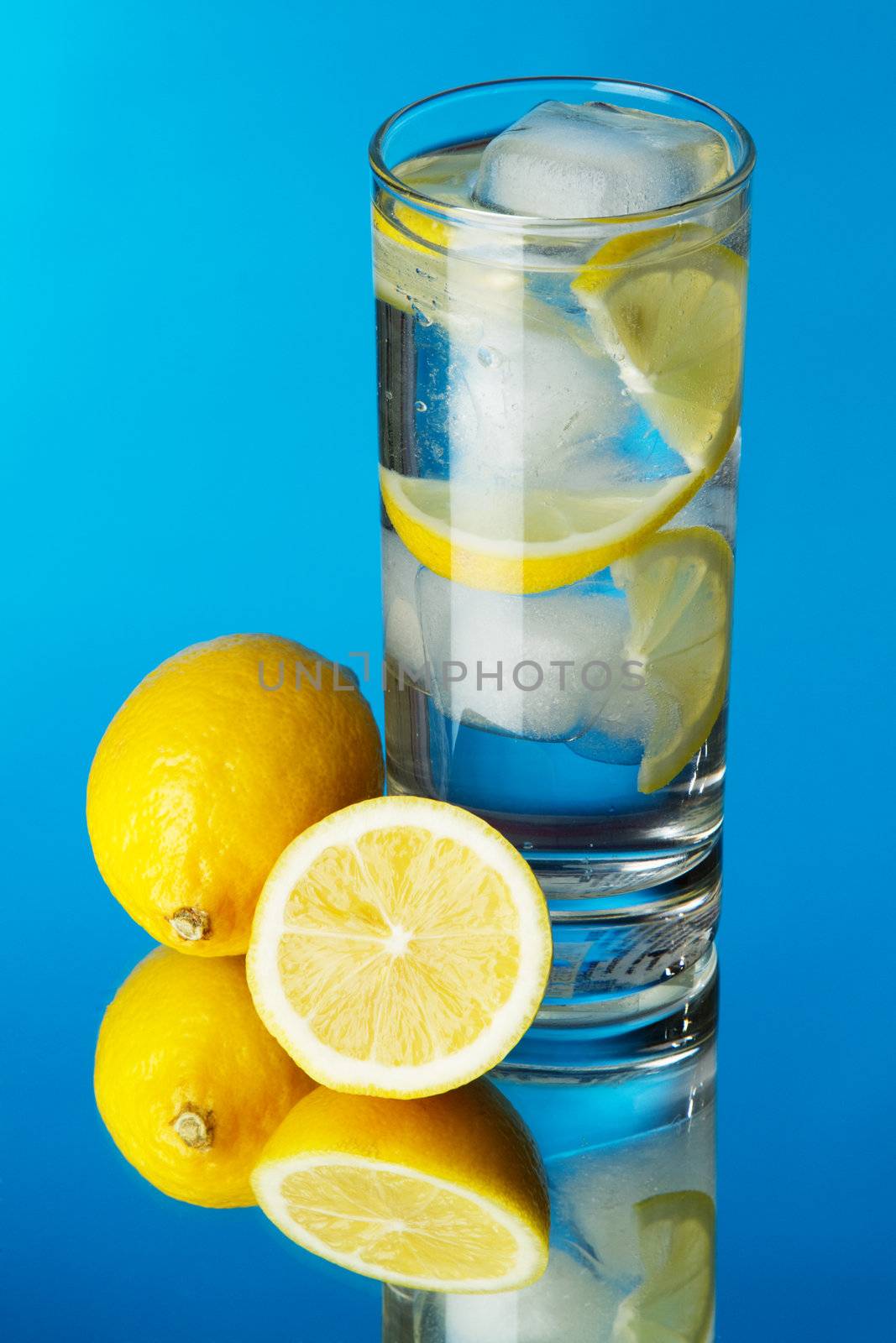 Glass of lemon ice water on blue background by Gdolgikh