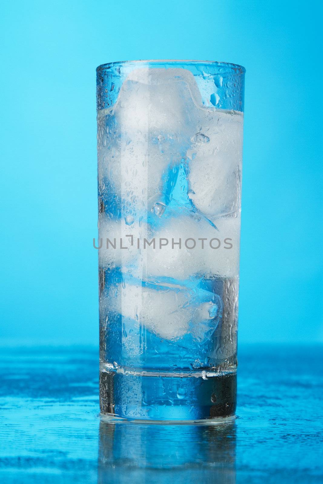 Glass of ice water on blue background, studio photo