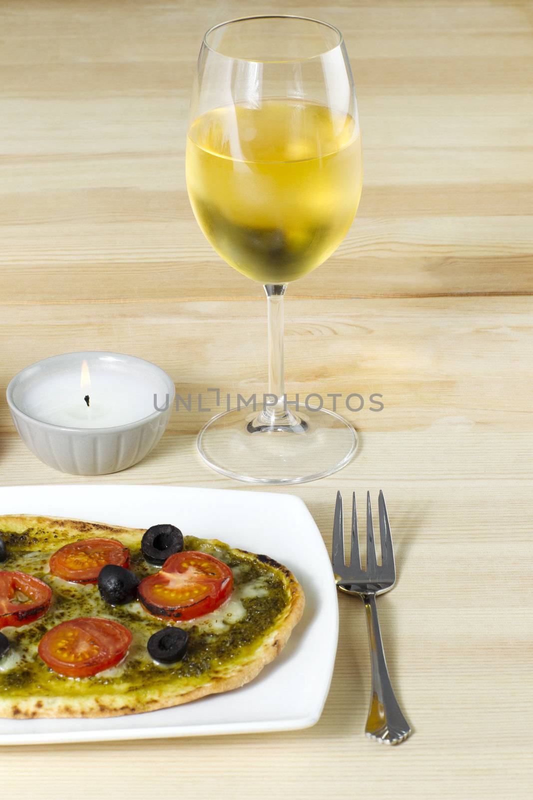 Baked pizza with wineglass and candle on table