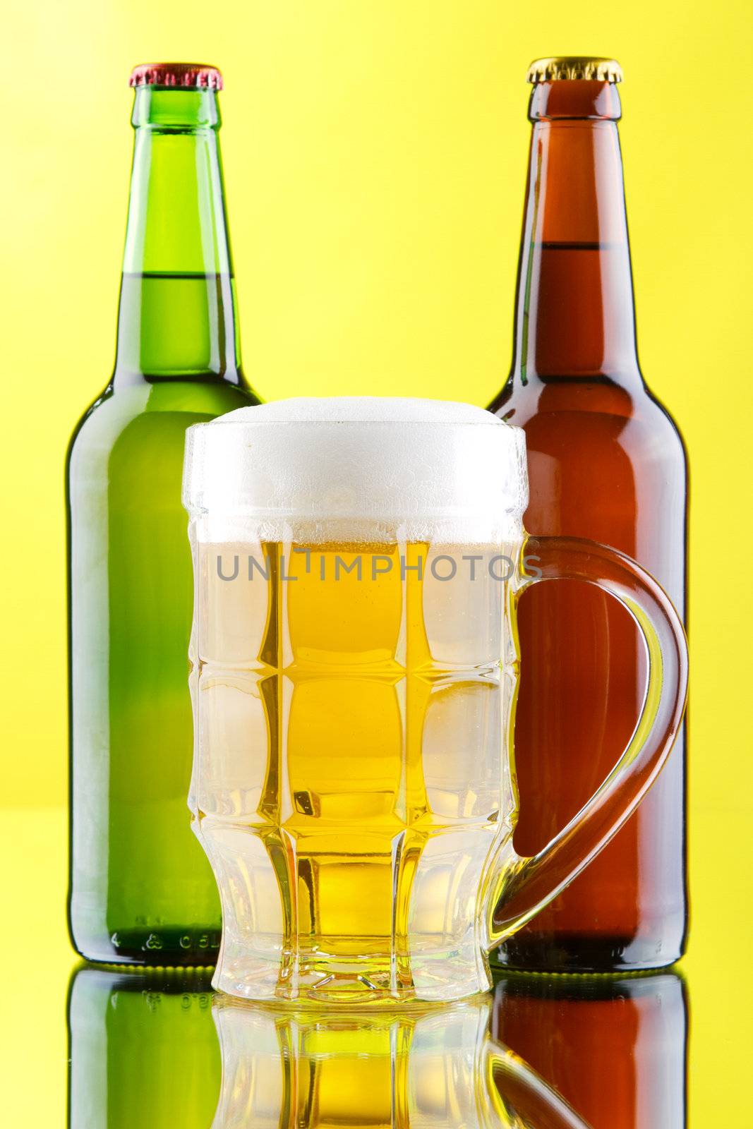 Beer mug and bottles on yellow background, studio photo