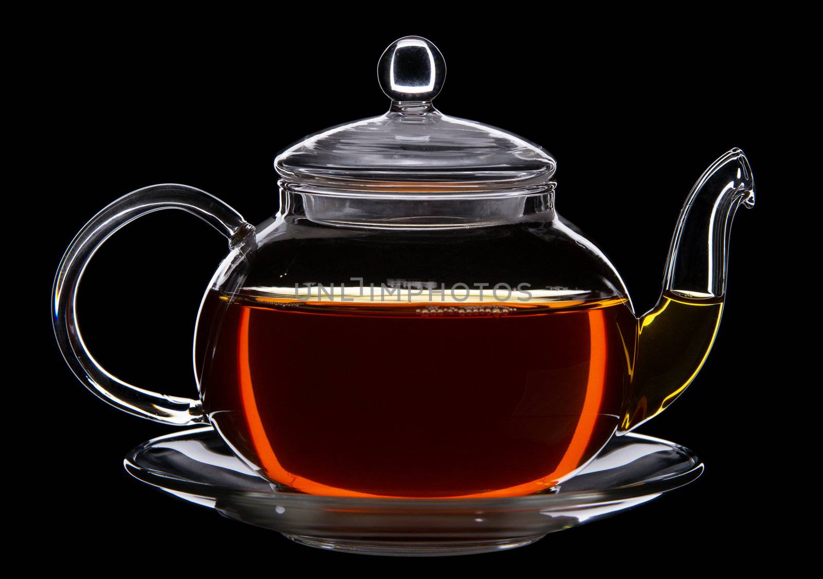 Glass teapot of black tea against black background