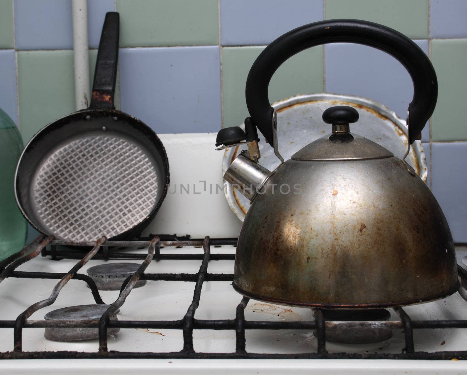 Dirty gas stove with teakettle and frying pan on it.