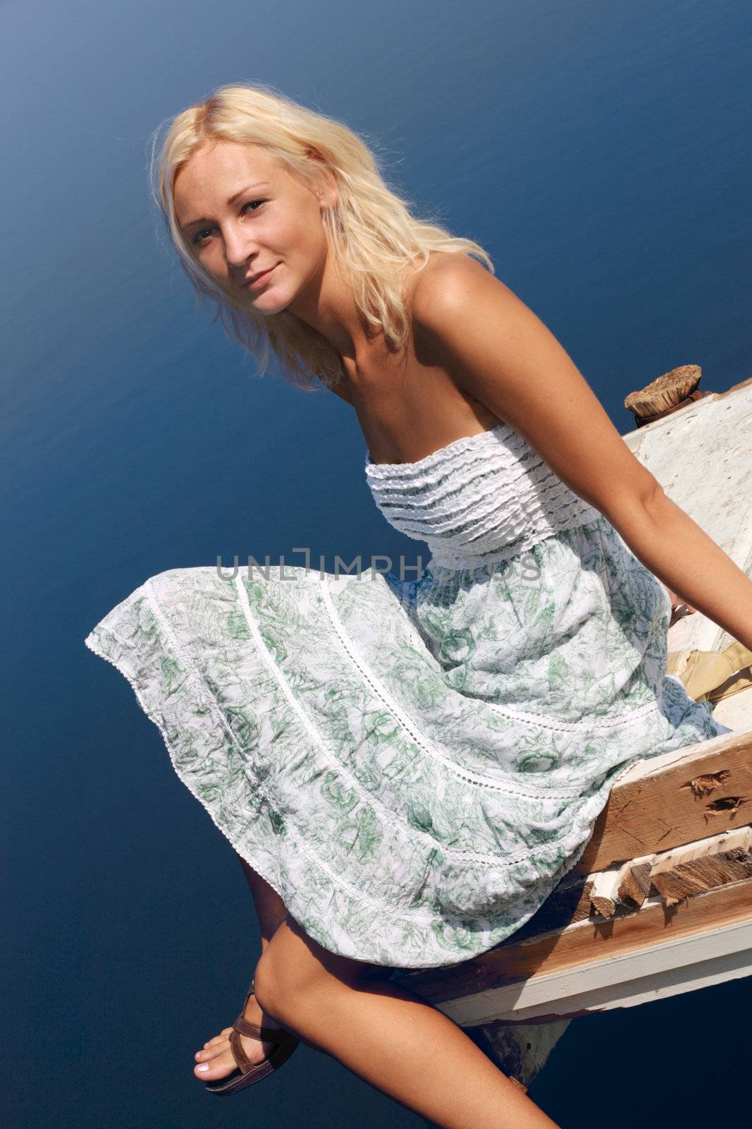 Girl dressed in a light summer dress, sitting on a pier at the river bank.