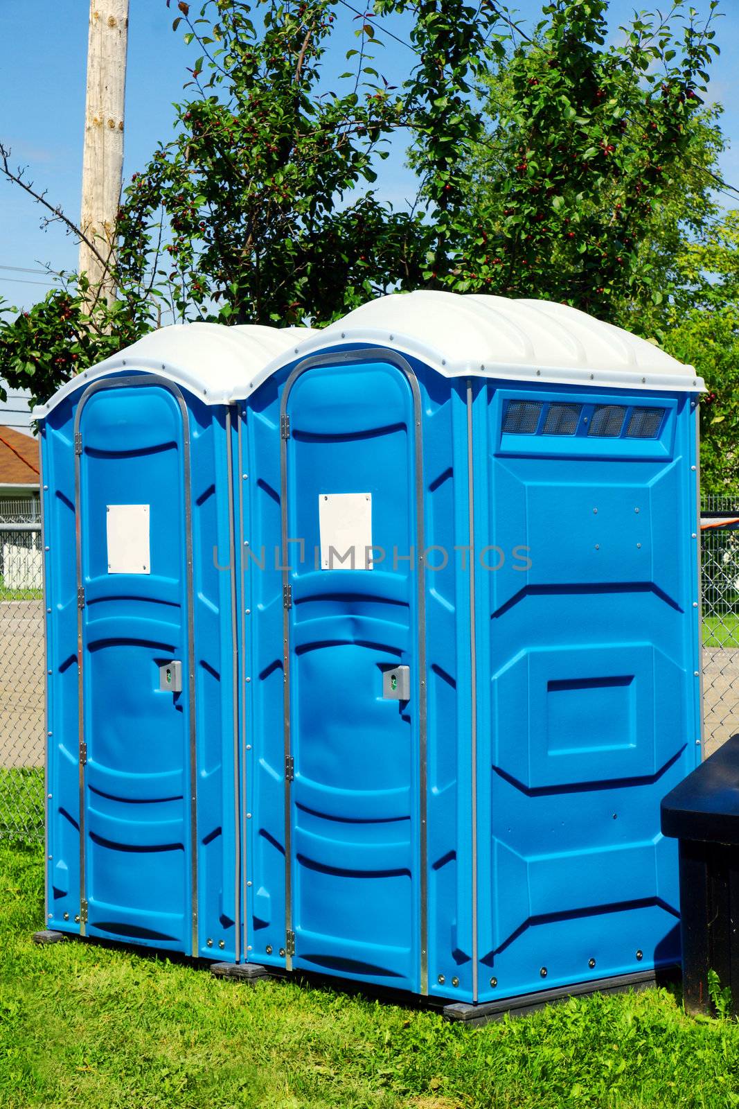 Two portable toilet or loo in blue plastic at a park public event or concert, with white sign on door ready for text.