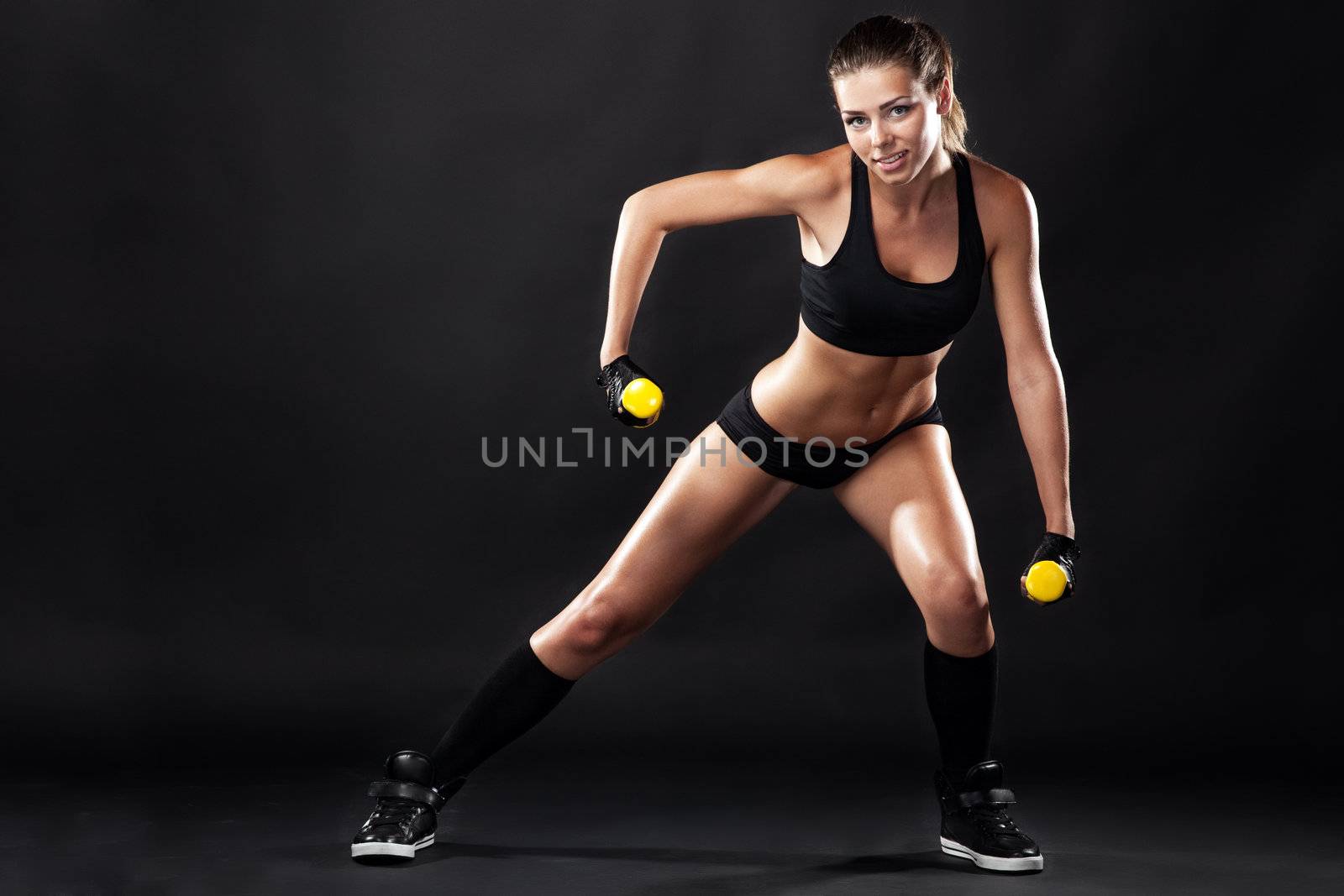 Beautiful slim woman with dumbbells, black background