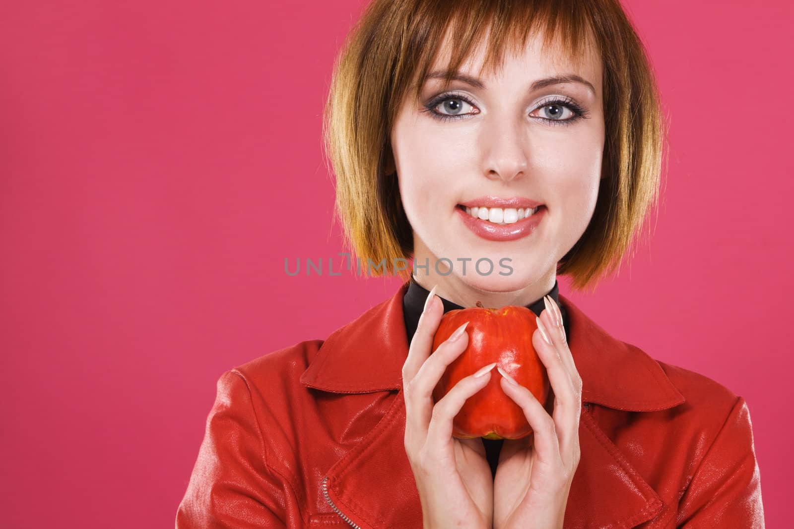 Portrait of a young beautiful woman with a red apple against pink background 