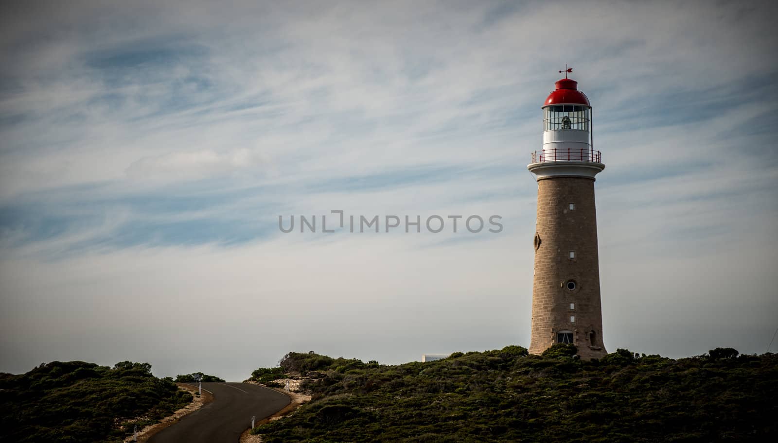 Winding road winds past a classic brick lighthouse with a traditional red and white top