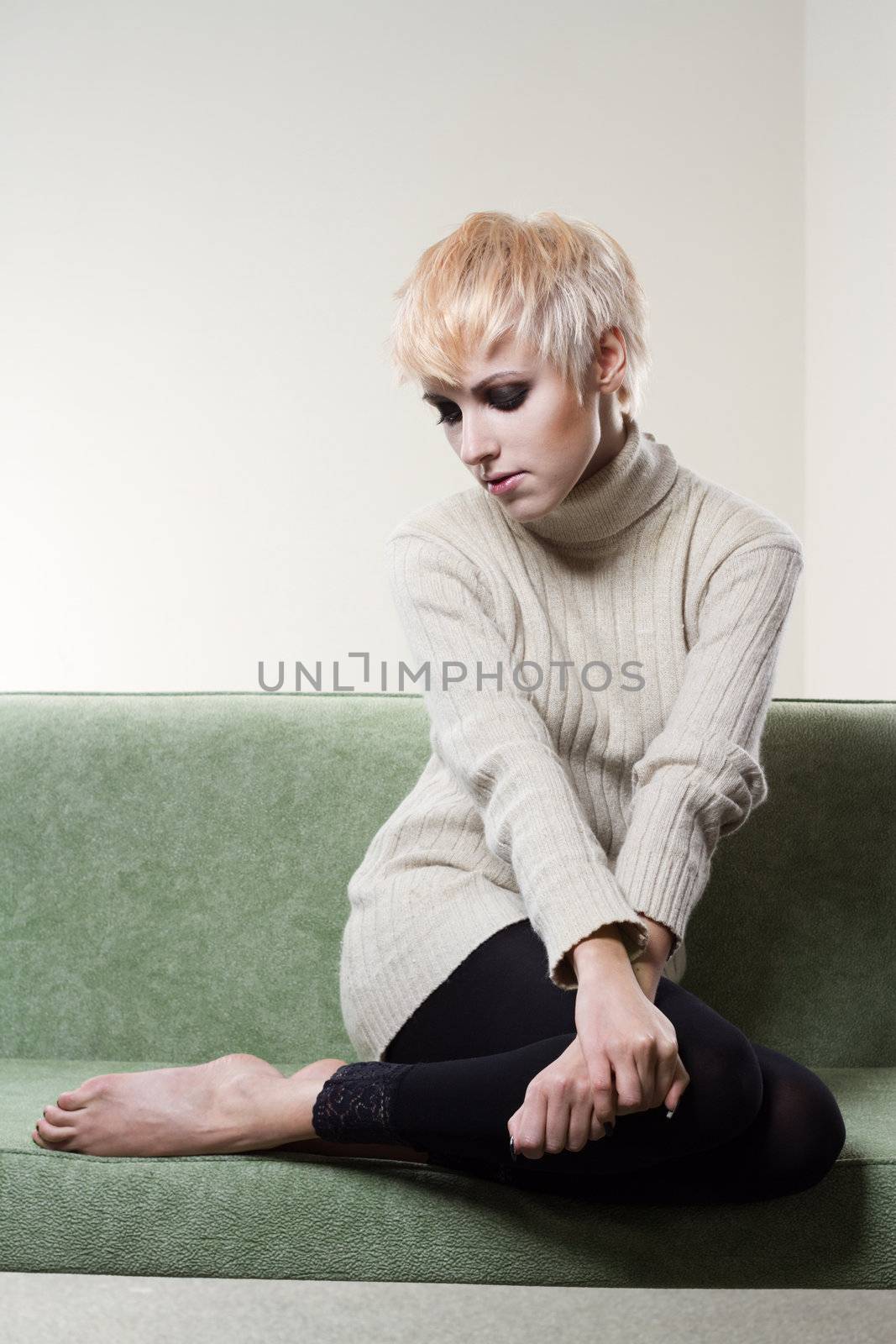 Young beautiful sad woman sitting on sofa by Gdolgikh