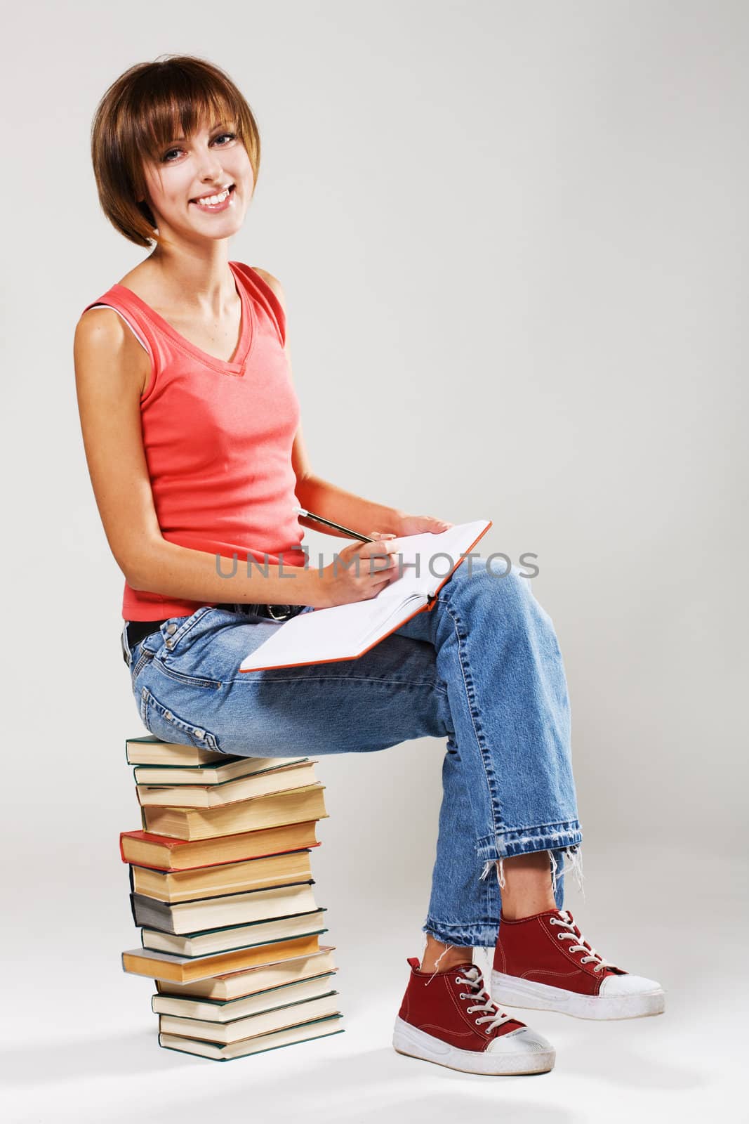 Lovely student sitting on a stack of books, gray background