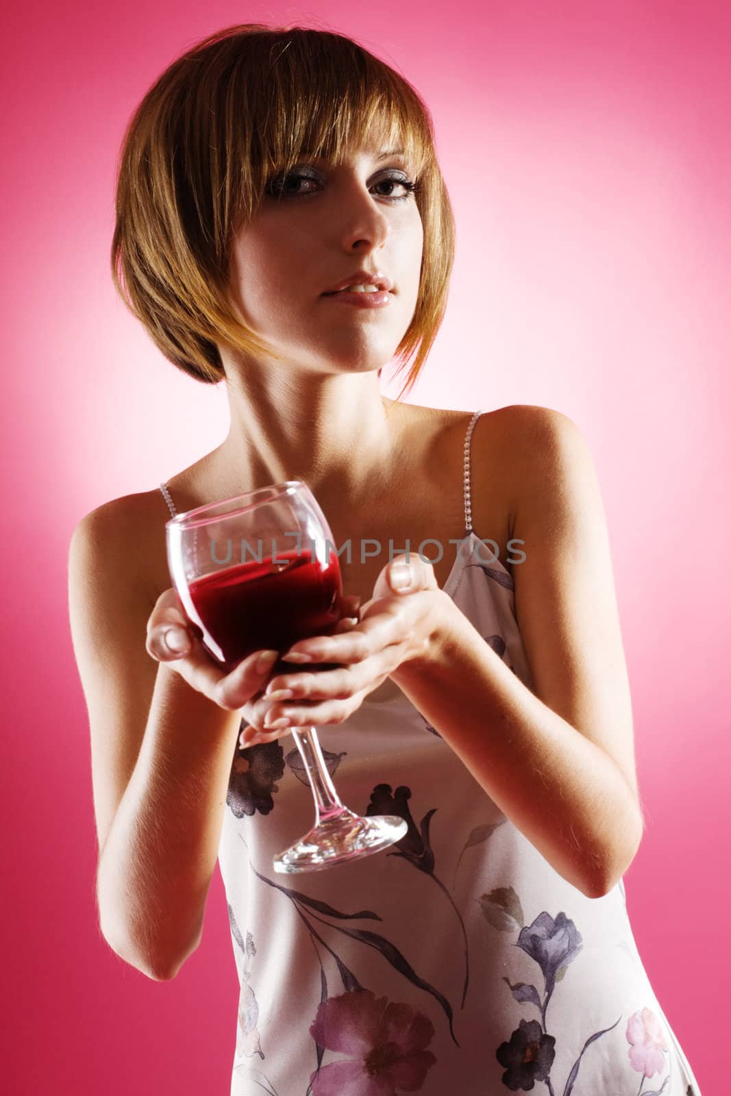 Portrait of a beautiful woman with a glass of wine against pink background 