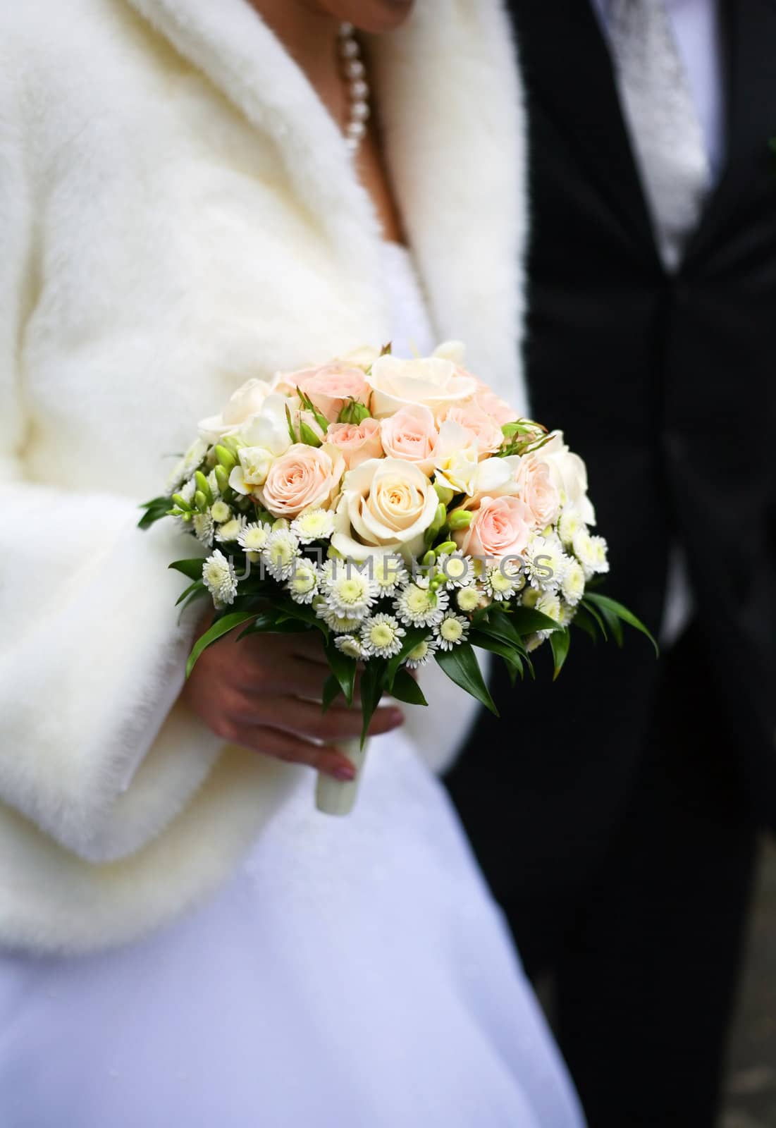 Bouquet of flowers on a background of a dress of the bride and a suit the groom.