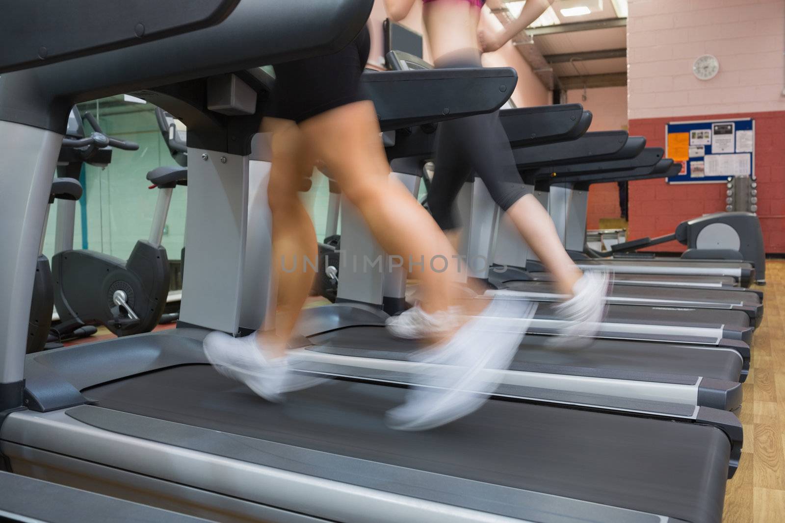 Two people running on treadmills in the gym side by side