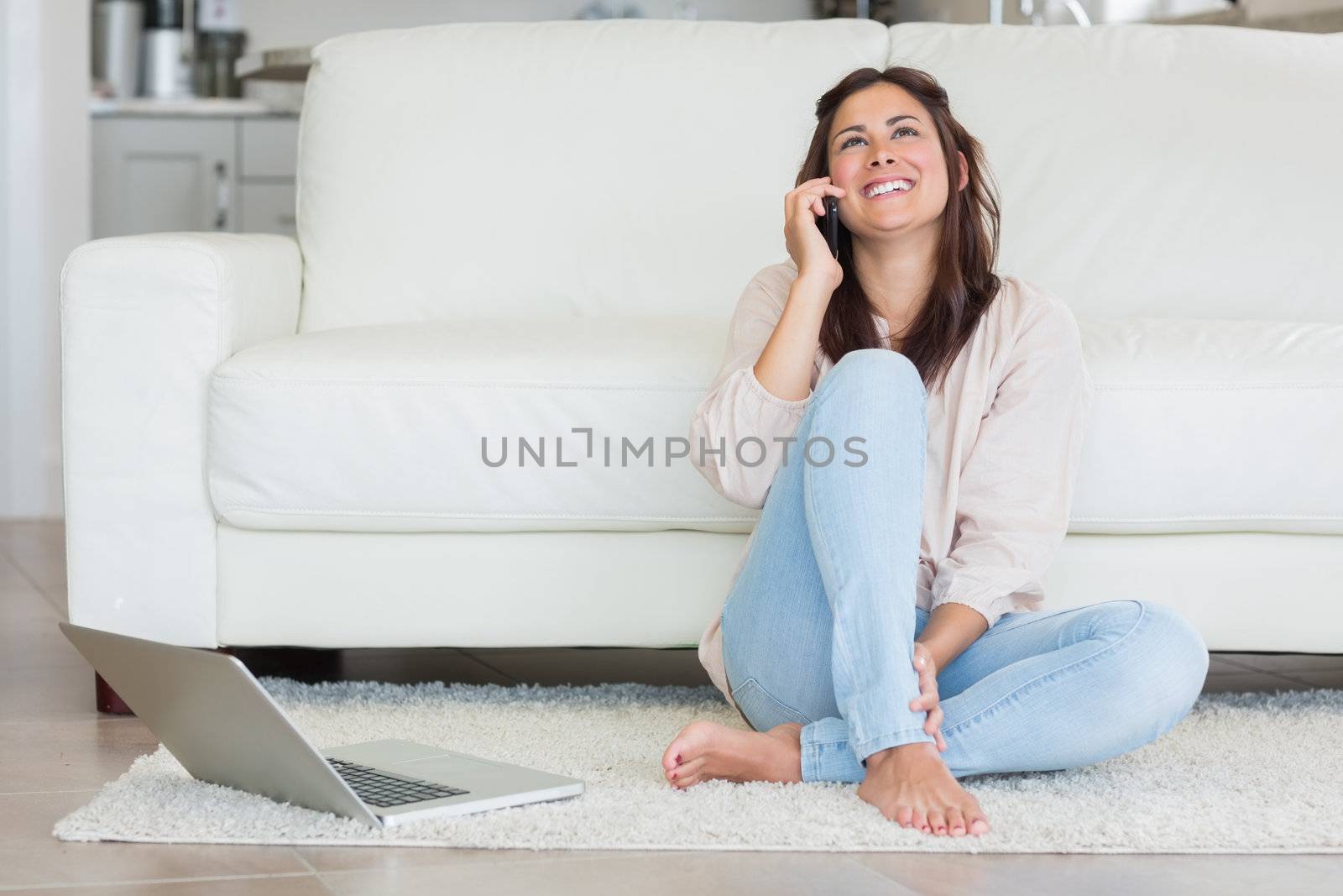 Smiling woman on the phone in front of laptop in living room