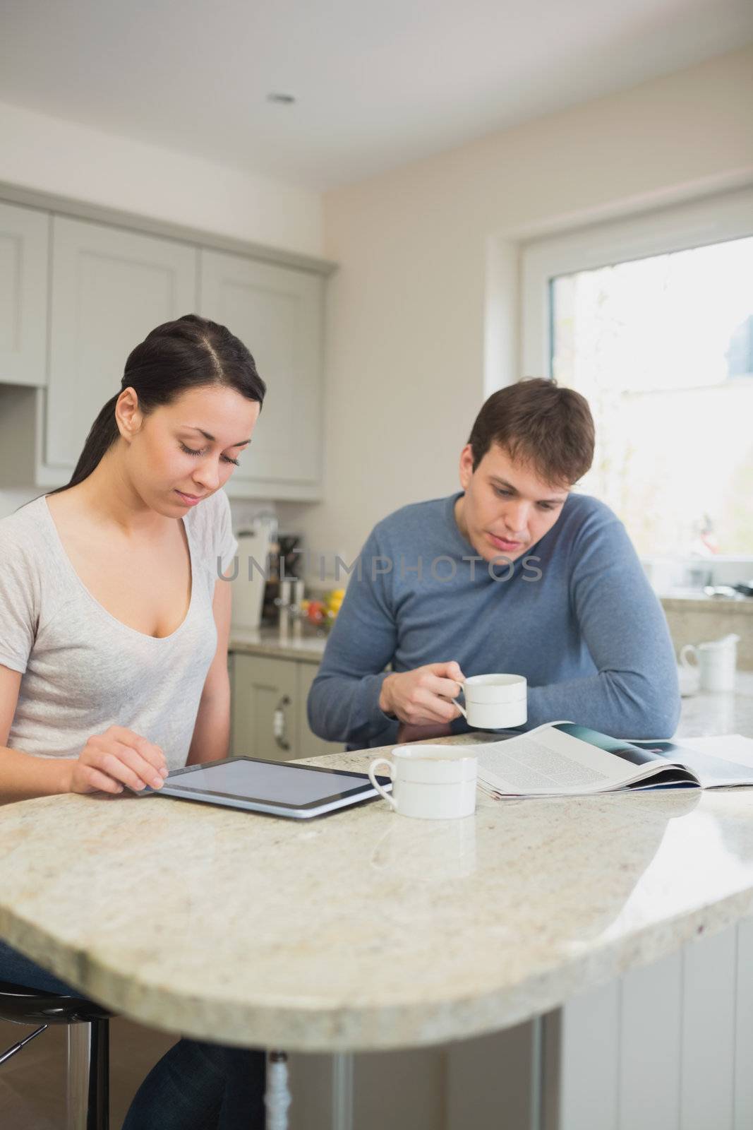 Two people reading from tablet pc and magazine in kitchen