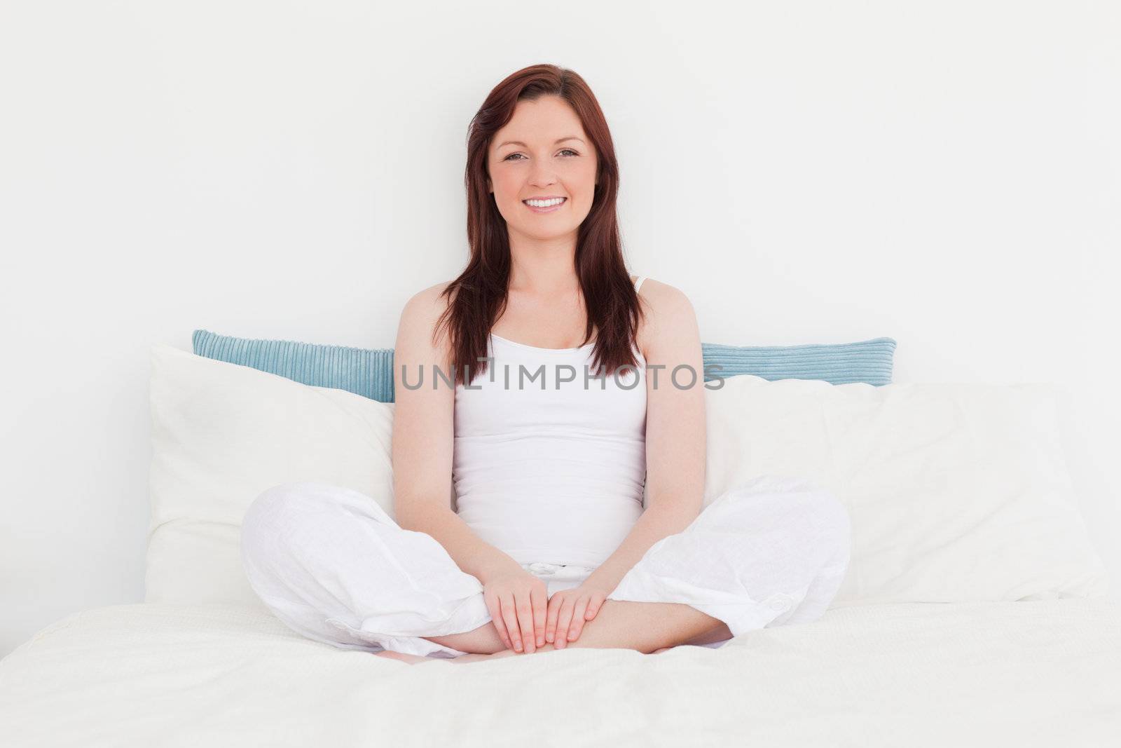 Good looking red-haired female relaxing while sitting on her bed by Wavebreakmedia