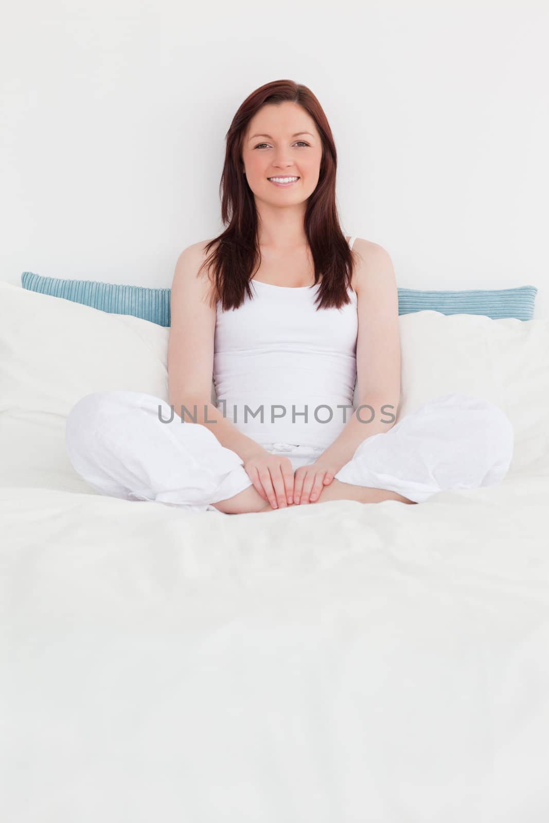 Pretty red-haired female relaxing while sitting on her bed