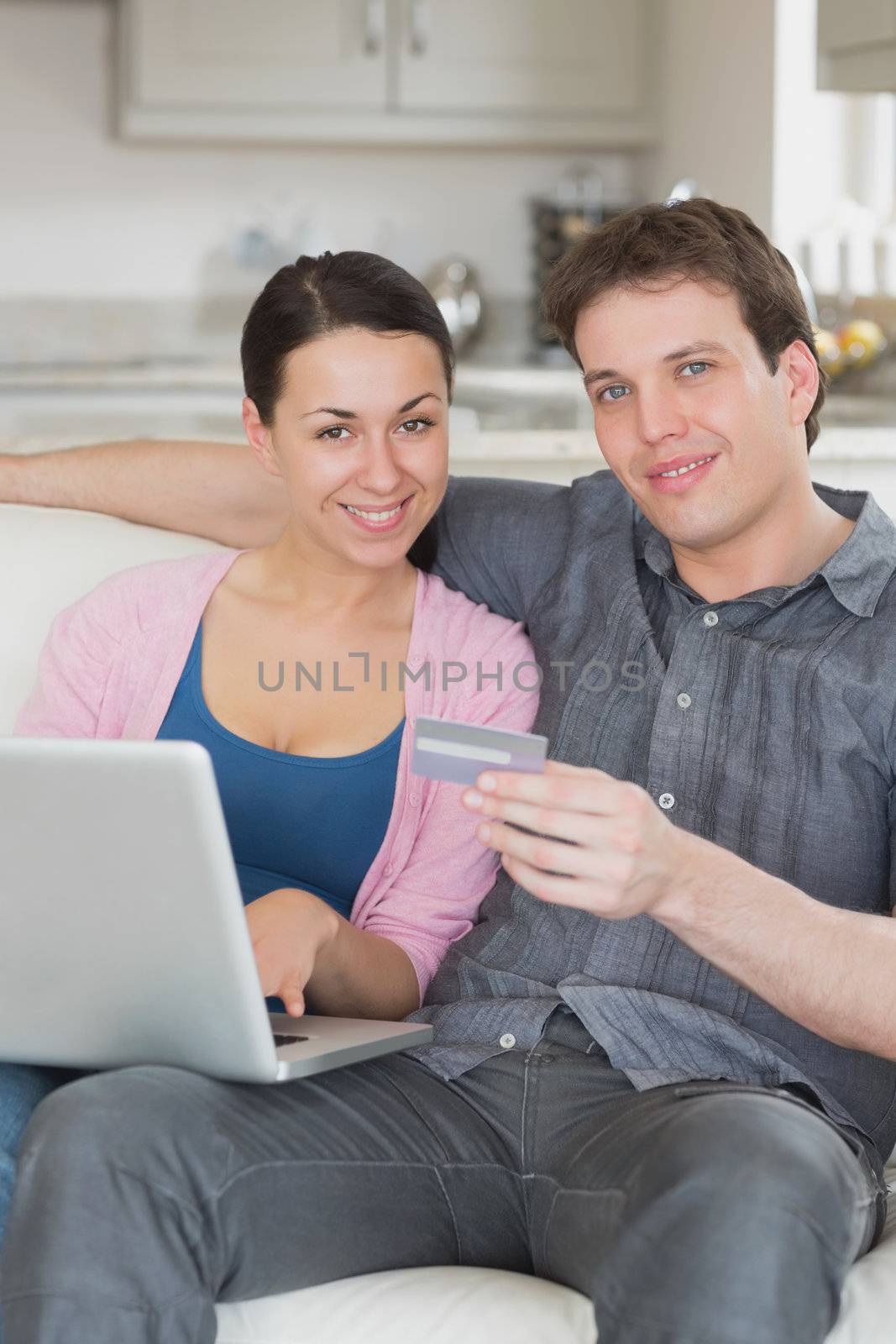 Couple sitting on the couch using the credit card while working on the laptop
