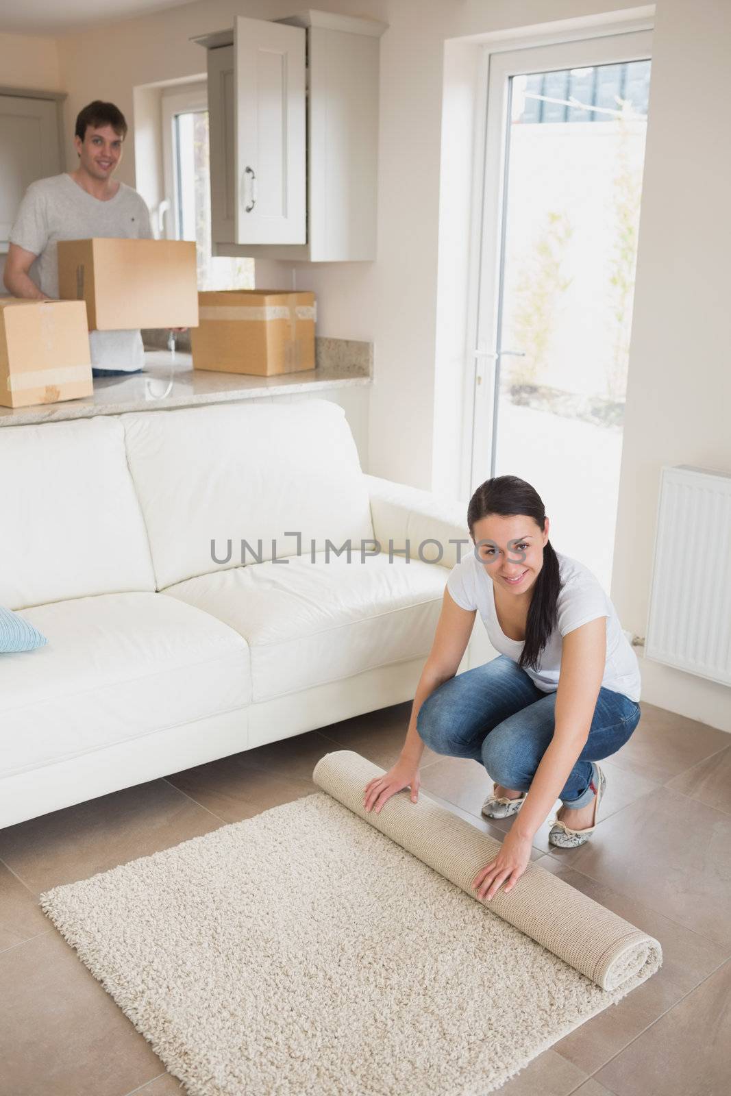 Two people furnishing the house while holding boxes and rolling out a carpet