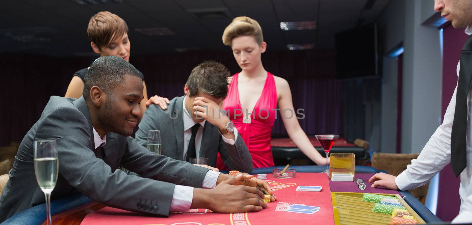 Women comforting man as other man takes jackpot at poker in casino