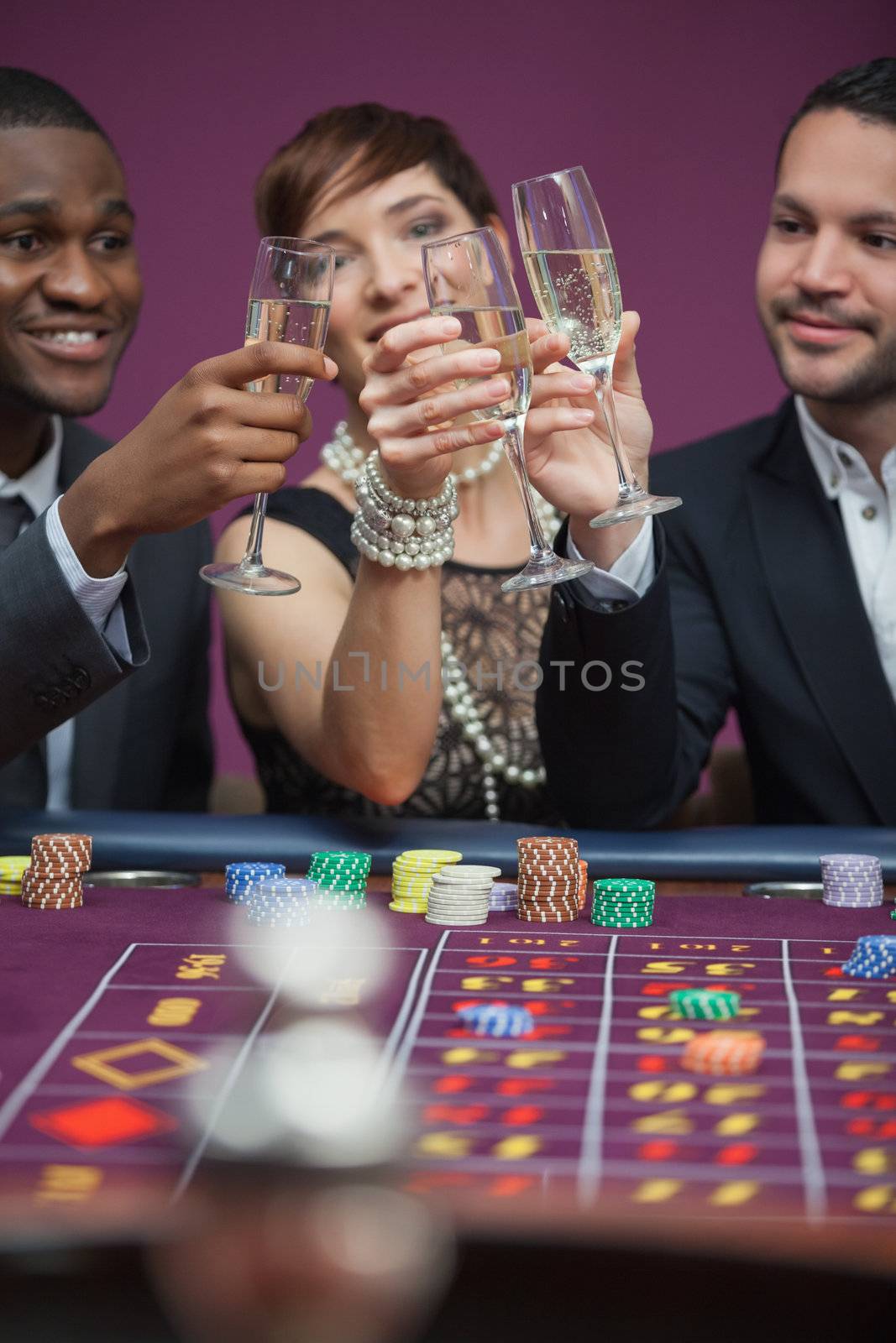 Three people toasting at roulette table in casino