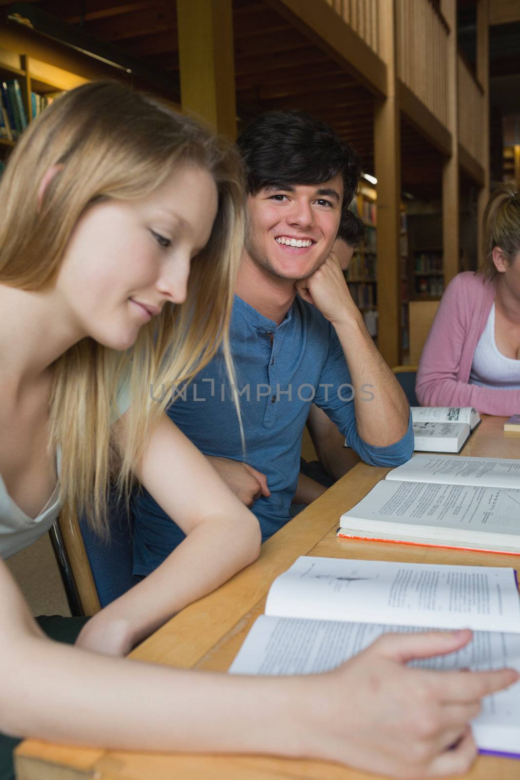 Male student looking up from study group and smiling in college library