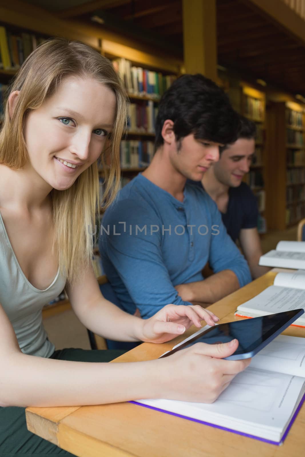 Woman holding a tablet pc sitting at the library by Wavebreakmedia