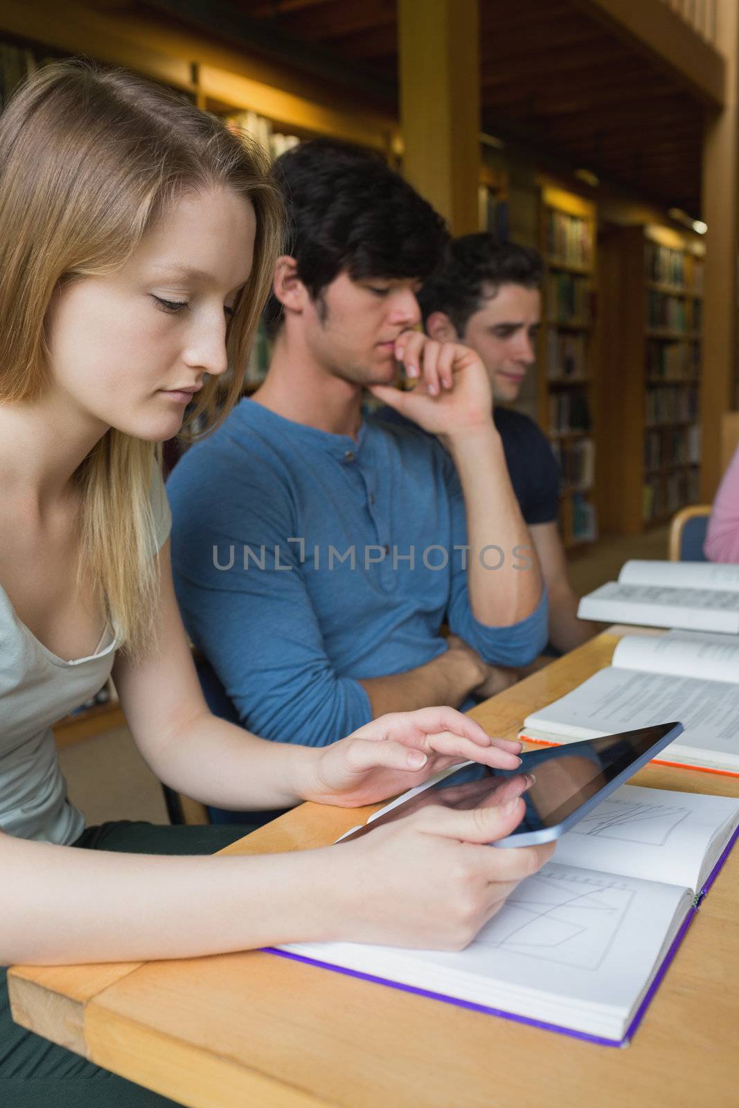 Woman in study group using tablet pc at desk in college library