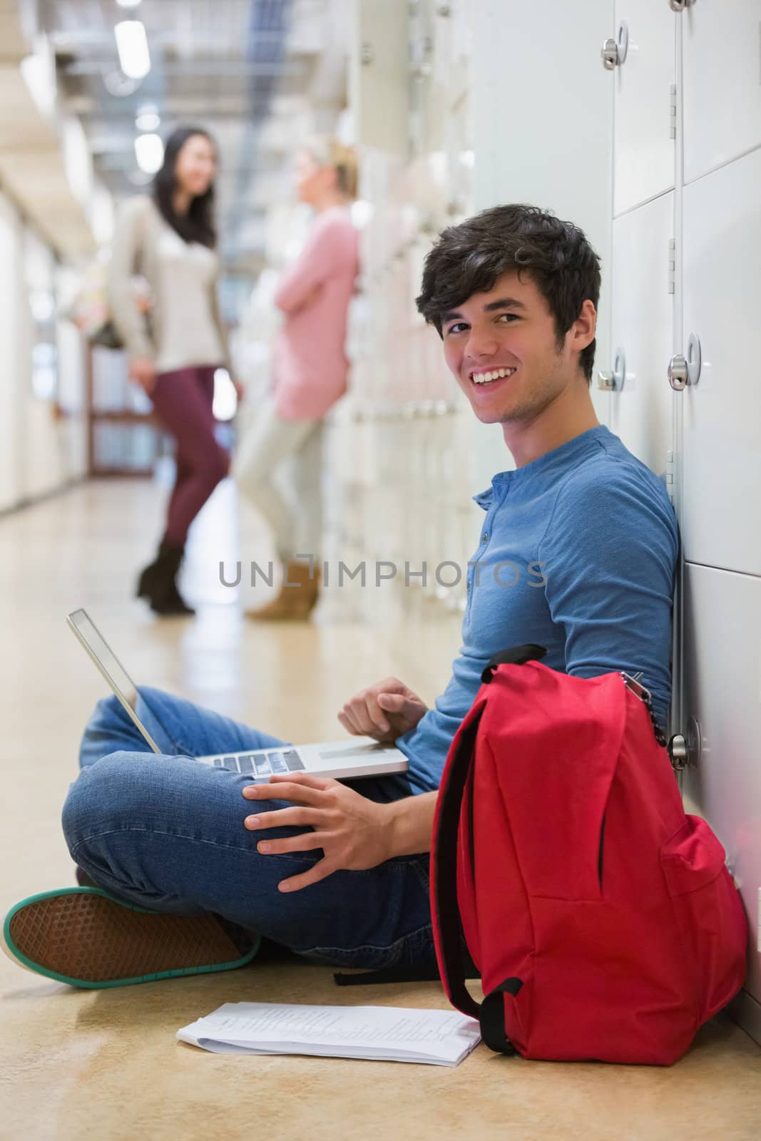 Man sitting on the floor at the hallway holding a laptop while smiling 