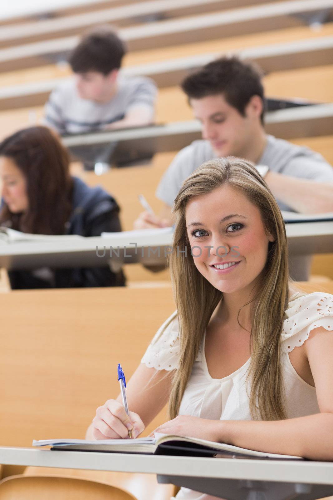 Woman sitting while smiling and taking notes by Wavebreakmedia