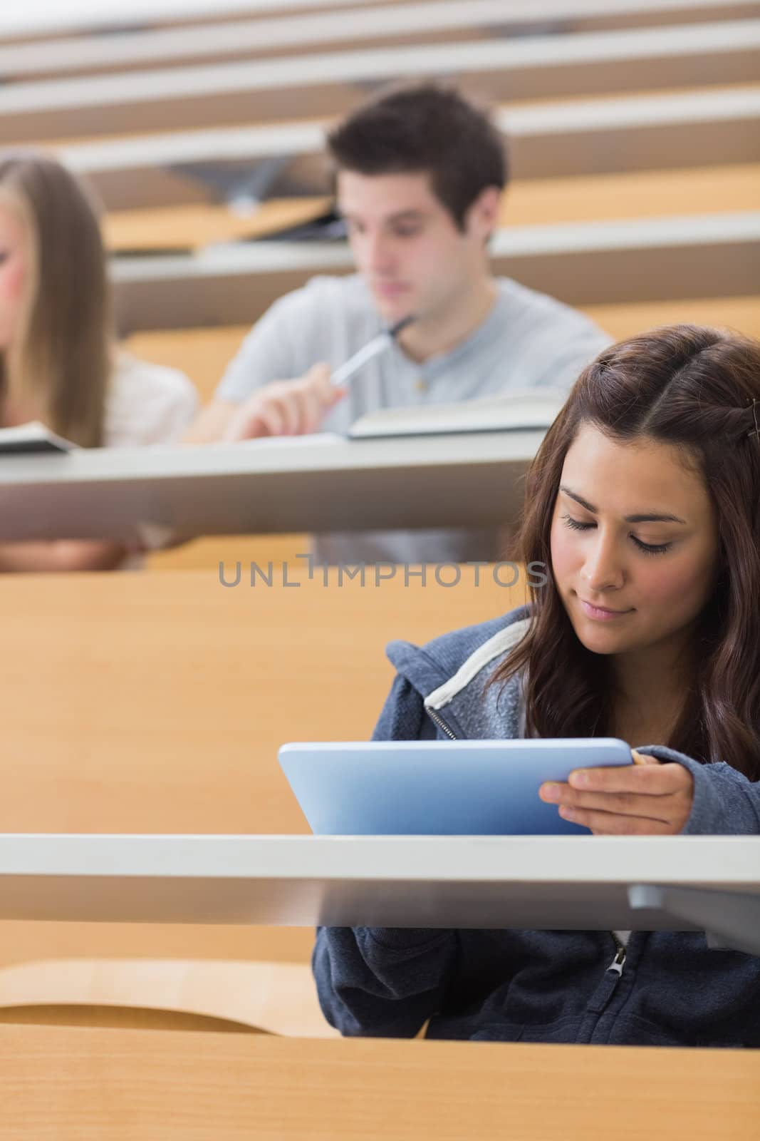 Woman sitting at the lecture hall holding a tablet computer and using it to take notes