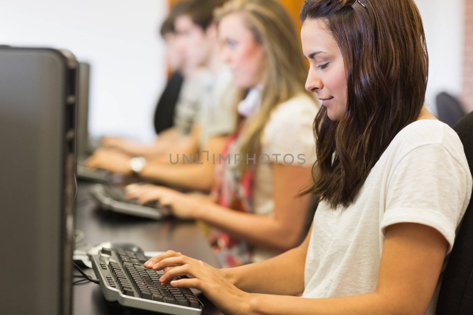 Woman looking at the keyboard typing in computer class in college