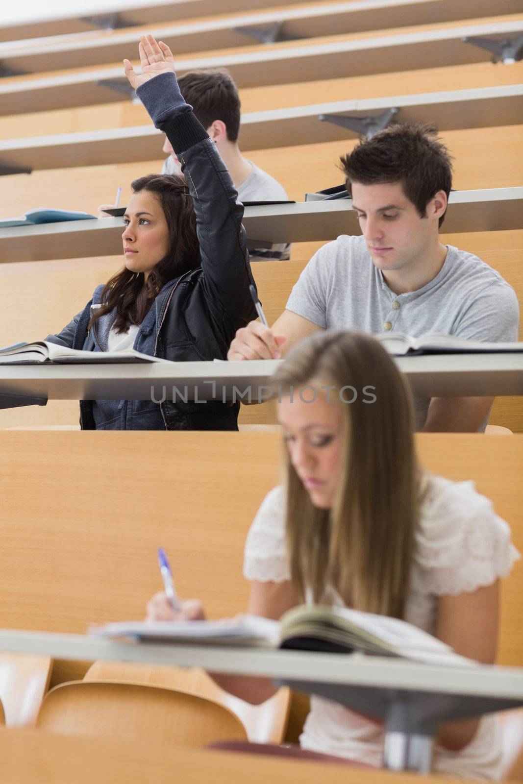 Student sitting at the lecture hall with hand up to ask question