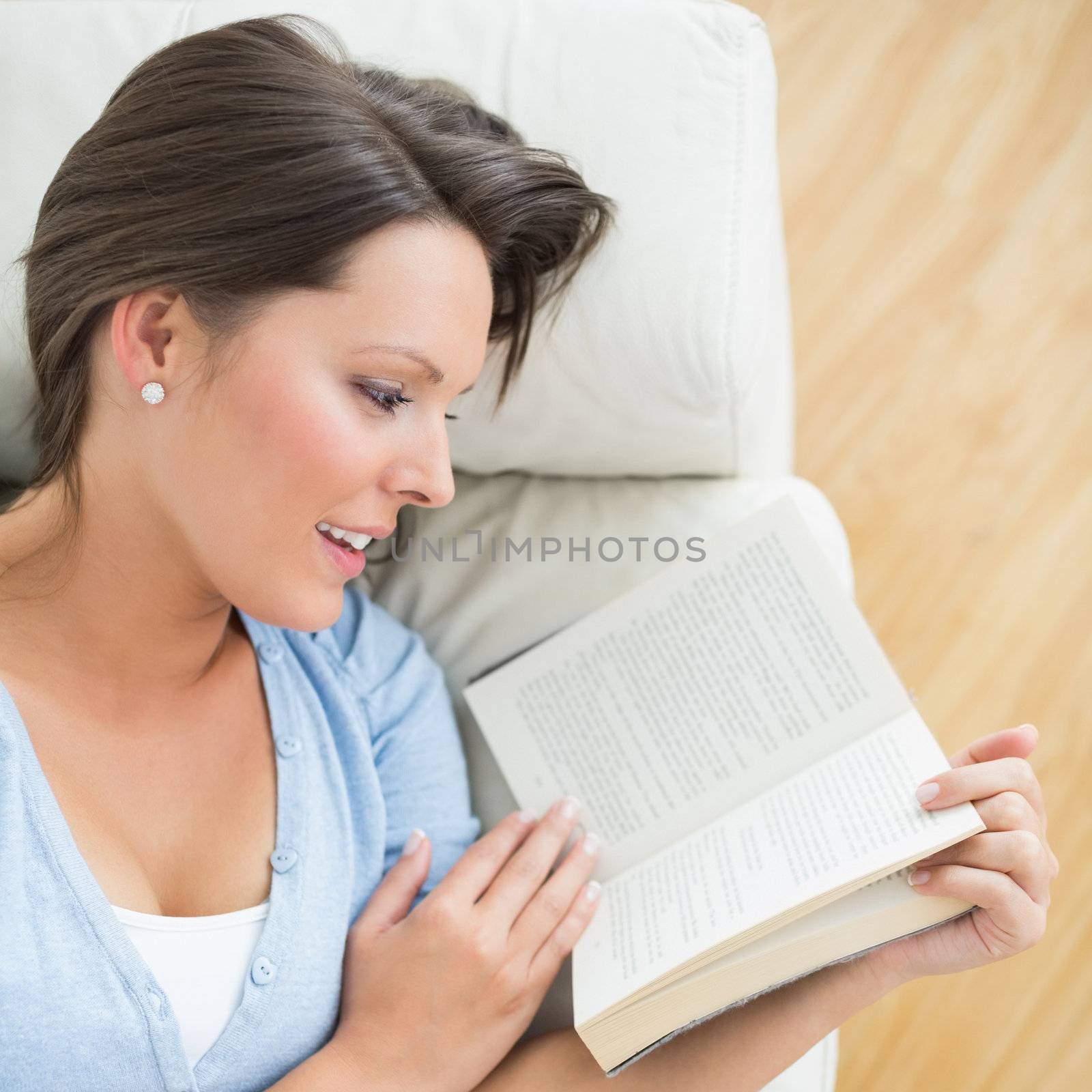 Smiling brunette reading a novel on the sofa by Wavebreakmedia