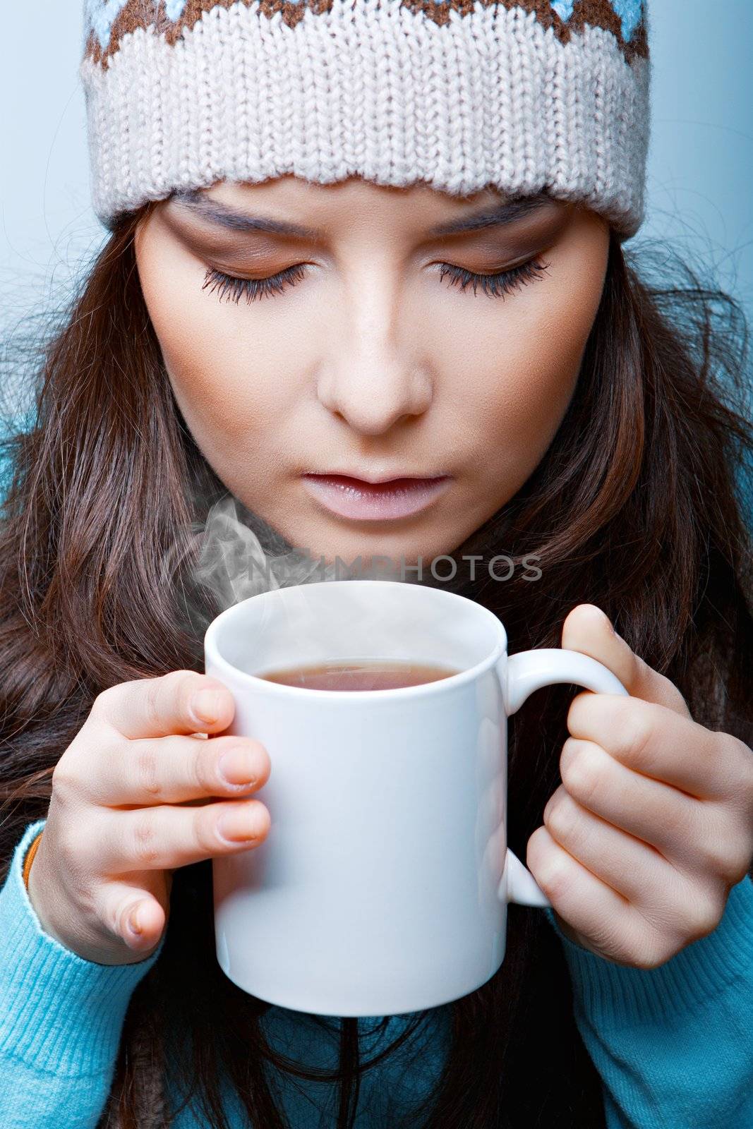 woman in a hat with hot tea closeup on a blue background
