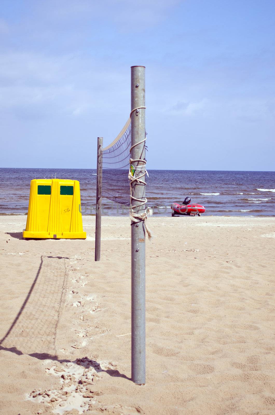 Volleyball net on sea sand yellow waste bin and lifeguard motor boat.