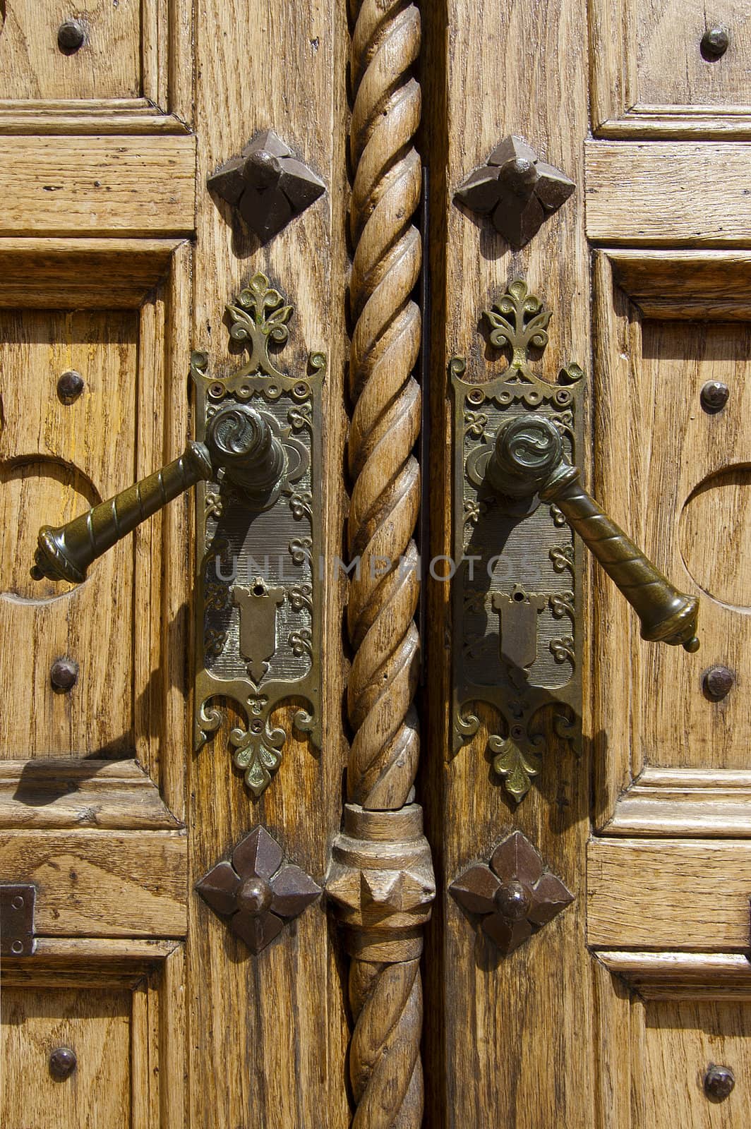 Closeup of old light wooden door of a church with two bronze handles
