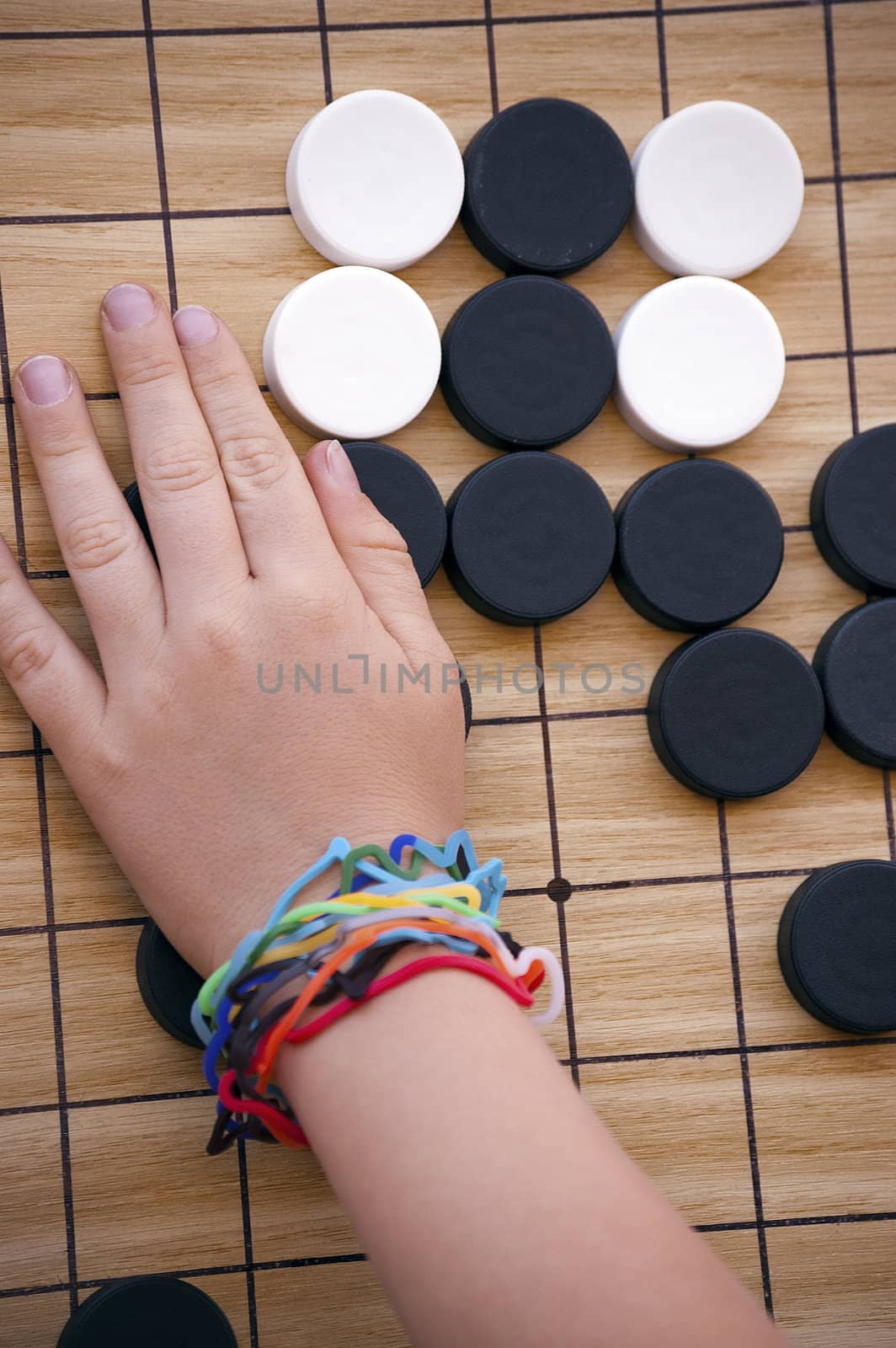 Child's hand playing with black and white checkers on wooden board
