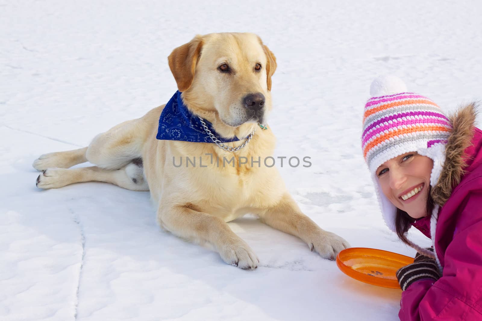 Happy pretty girl laying with her dog in snow on frozen lake
