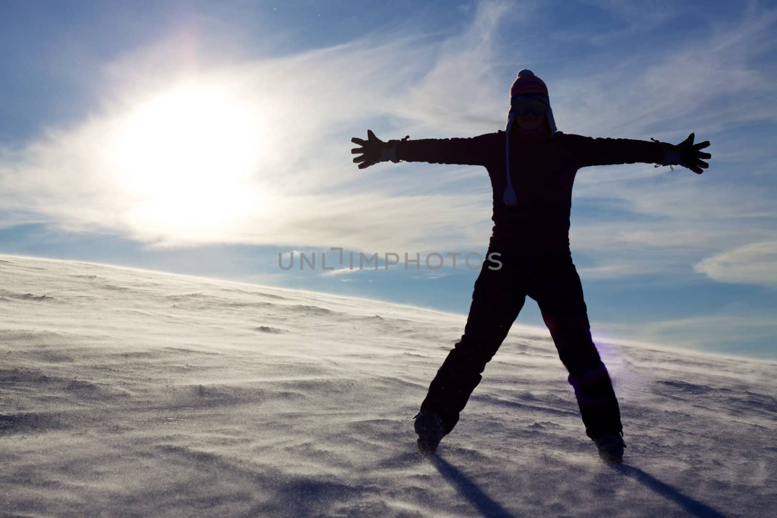 Silhouette of girl in snow spreading hands with sun in the background