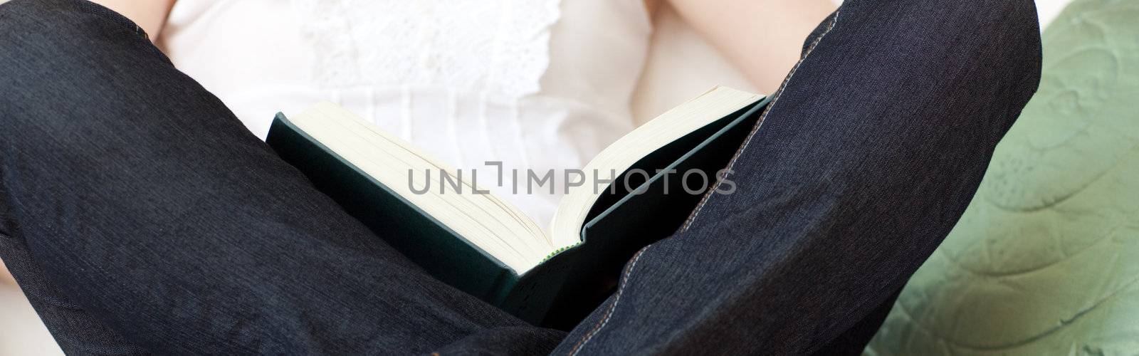 Close-up of a woman reading a book sitting on a sofa by Wavebreakmedia