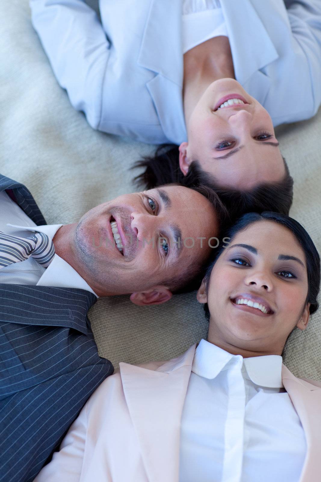 Business team on floor with heads together smiling by Wavebreakmedia