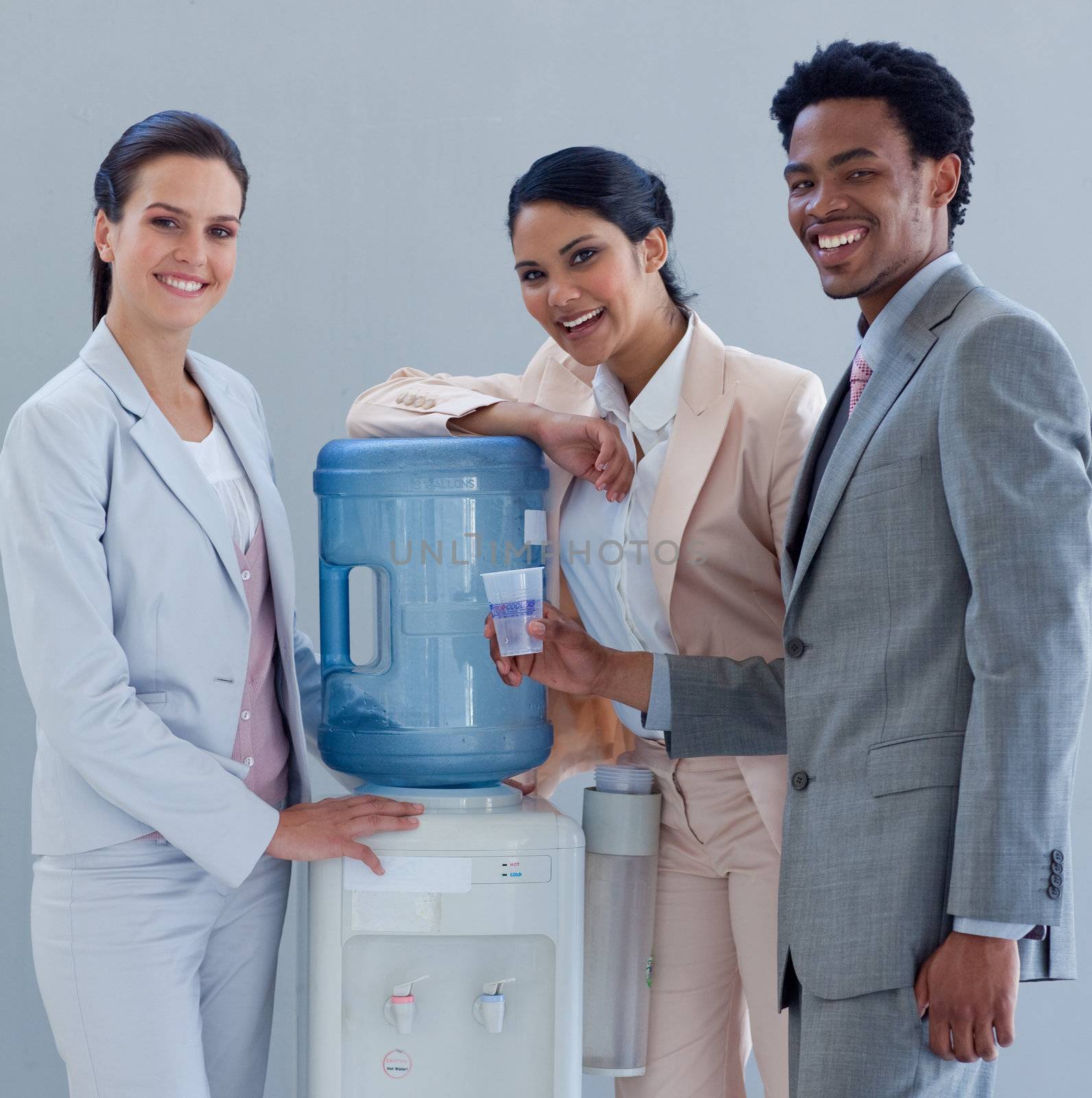 Smiling business people speaking next to a water cooler in office