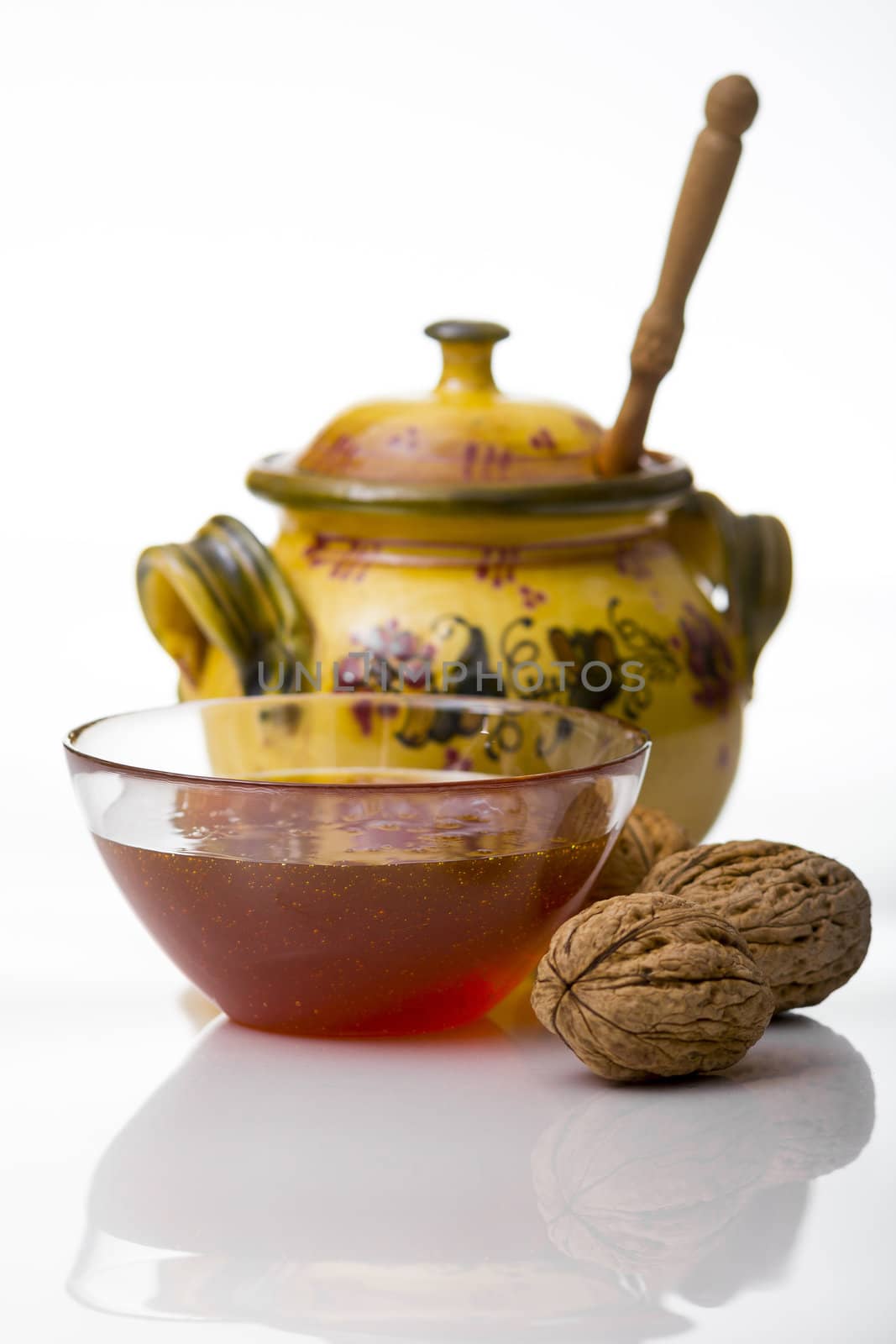 Transparent mug full of honey, honey jar and walnut on white background

