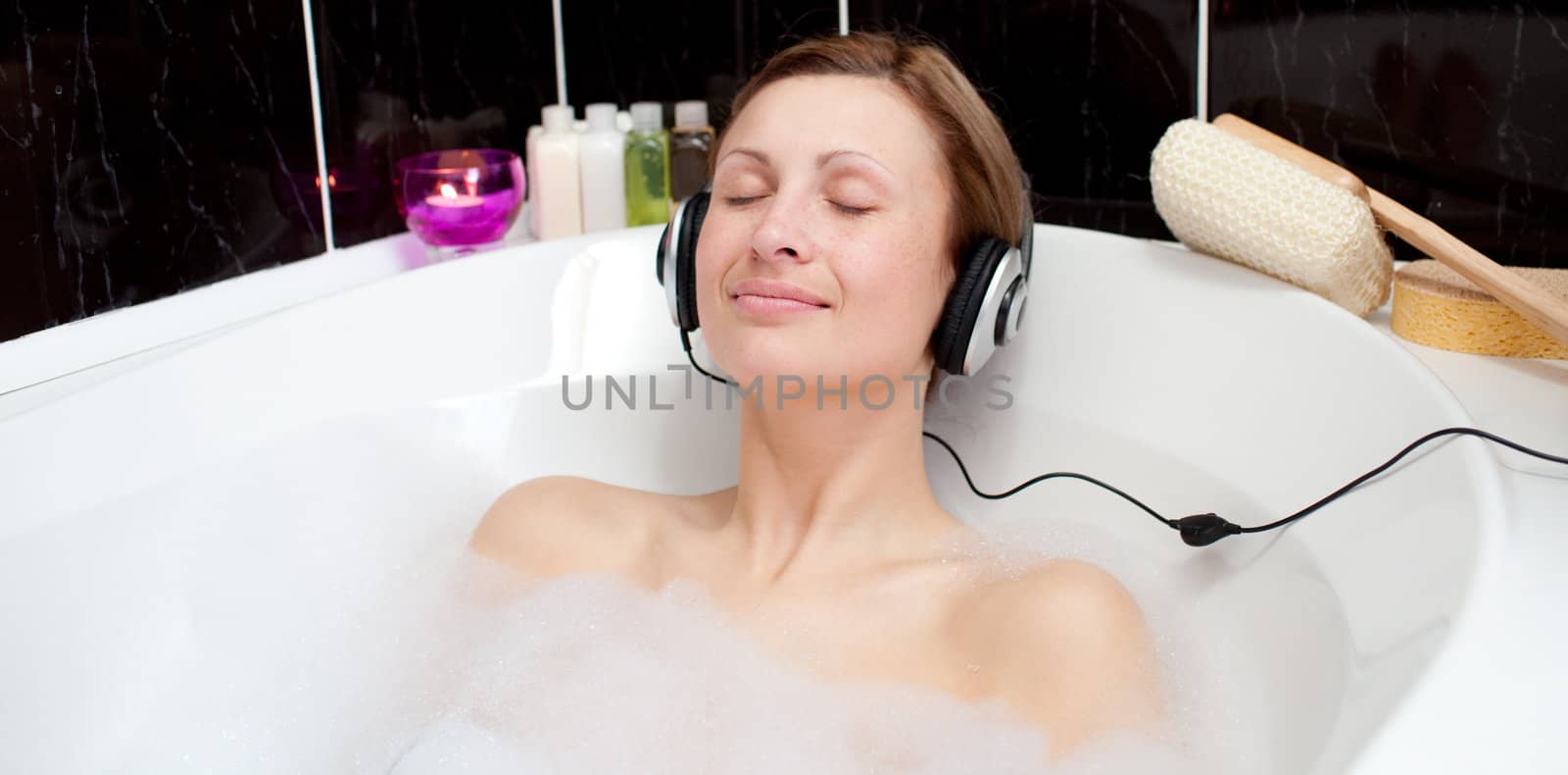 Relaxed woman listening music with headhones in a bubble bath 
