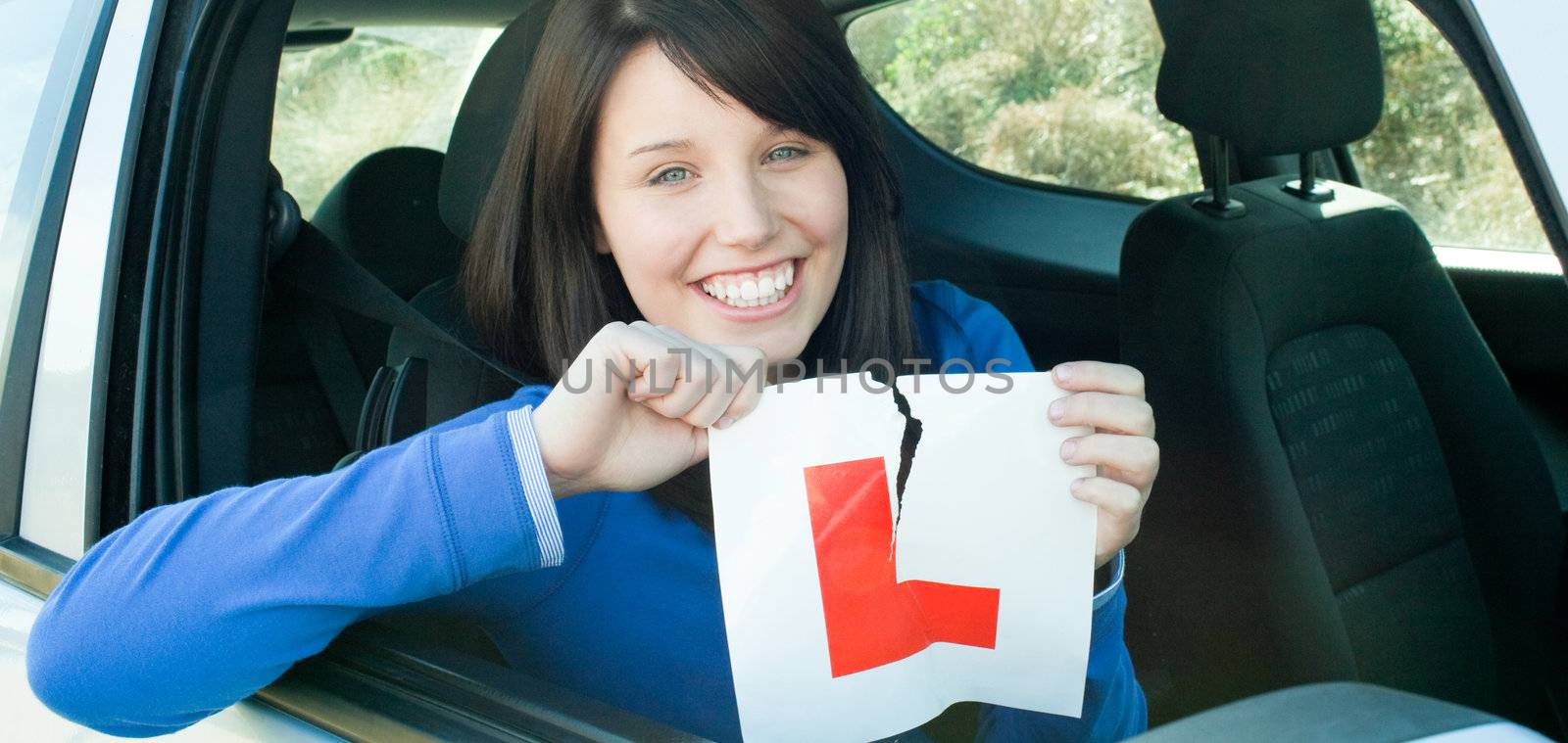 Smiling teen girl sitting in her car tearing a L-sign after having her driver's licence 