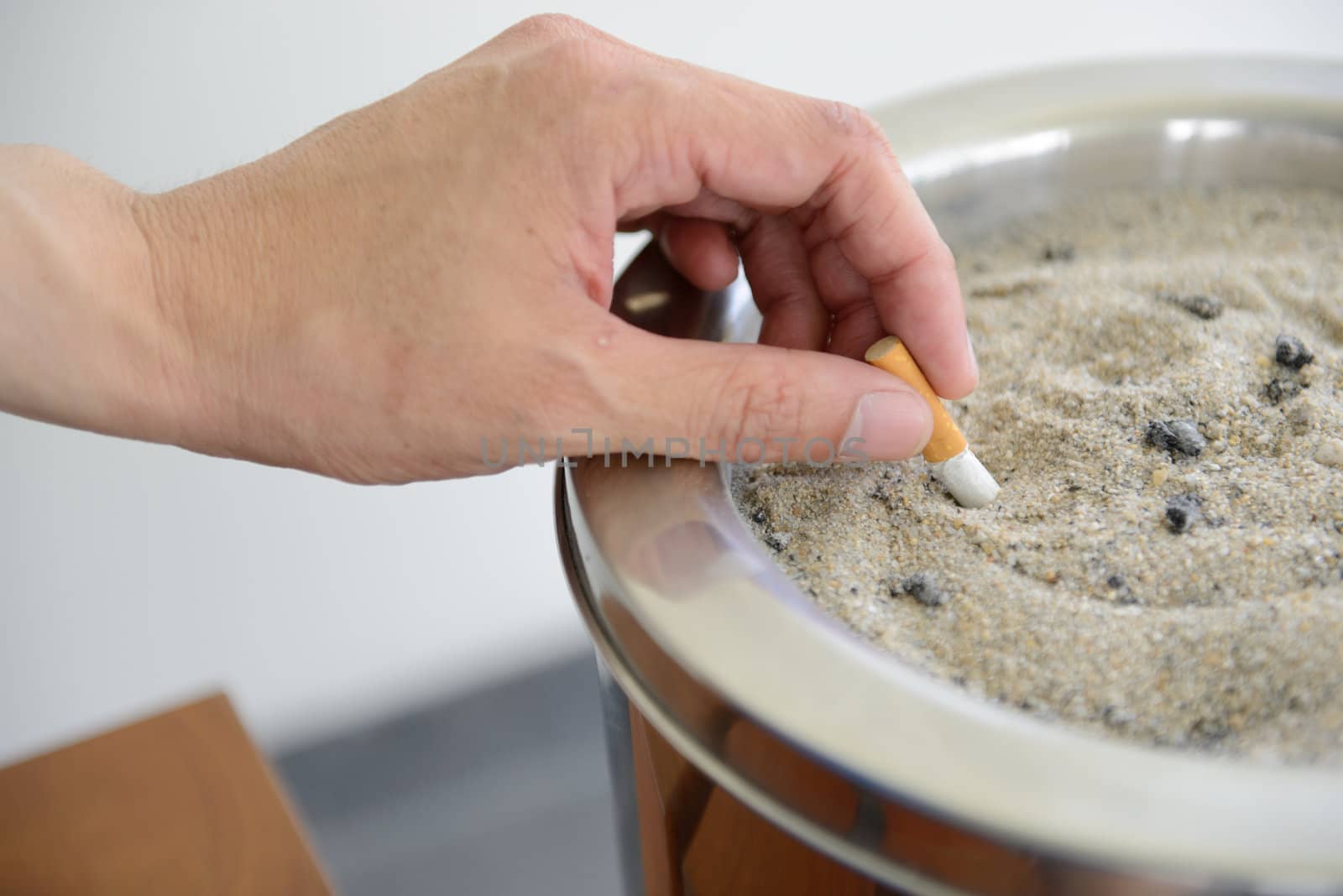 Closed up male hand Stubbing Out Cigarette in sand ashtray bin