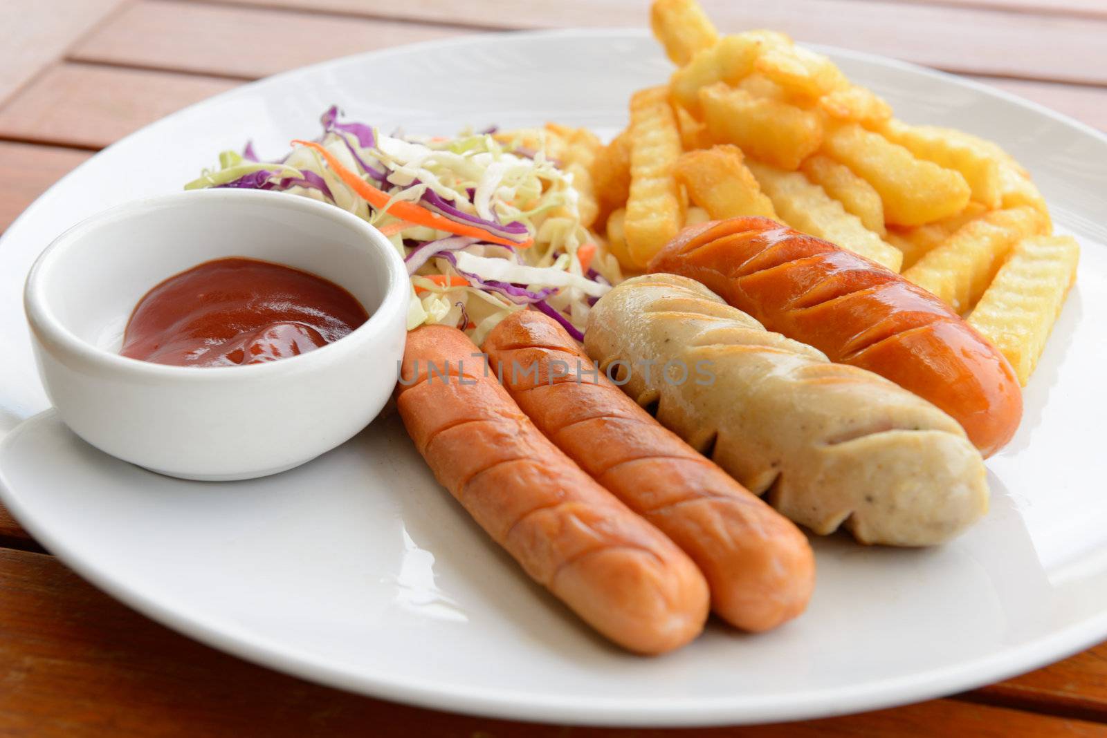 Mixed sausage served with french fried in the white dish put on the wood table