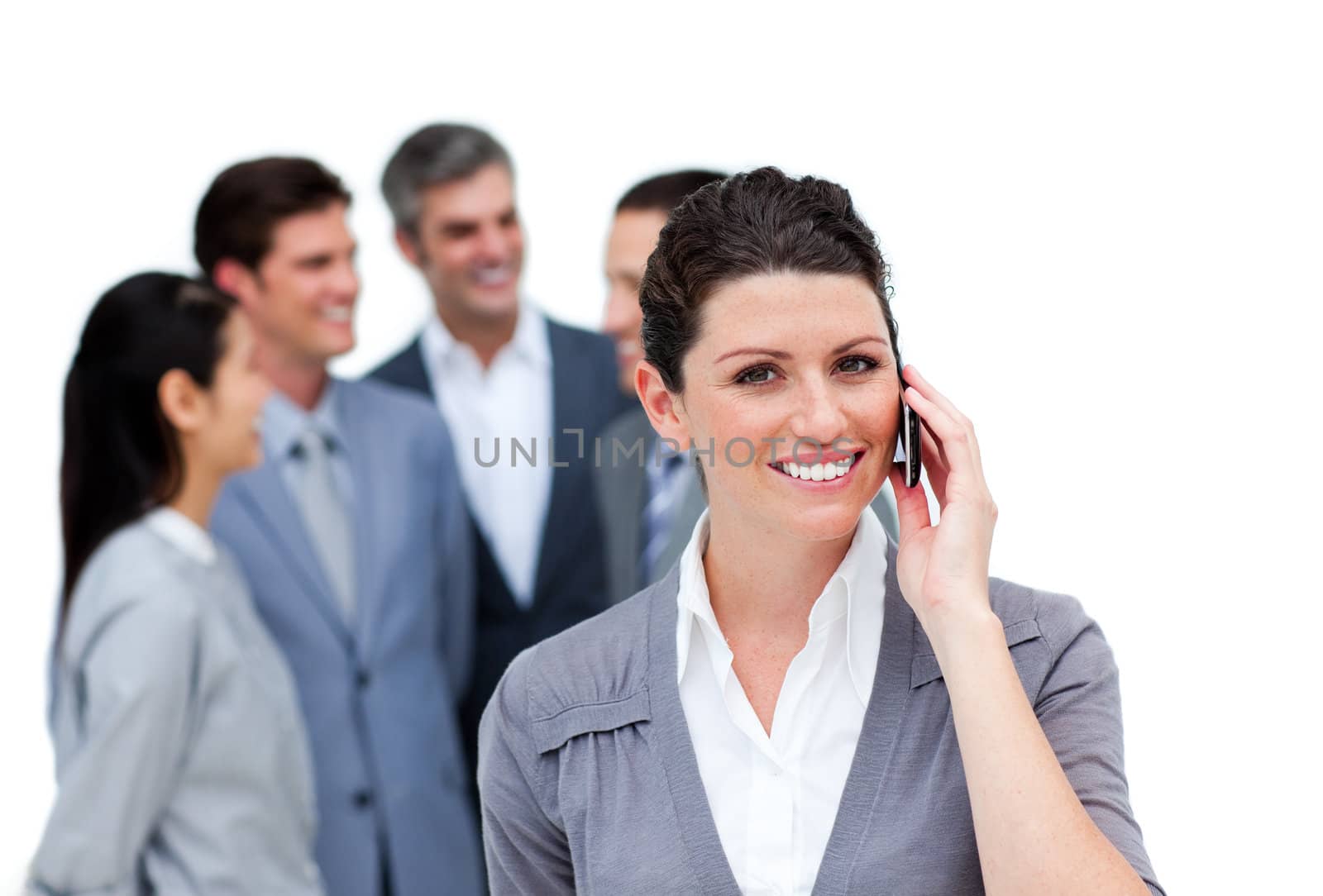 Brunette woman talking on phone in front of her team against a white background