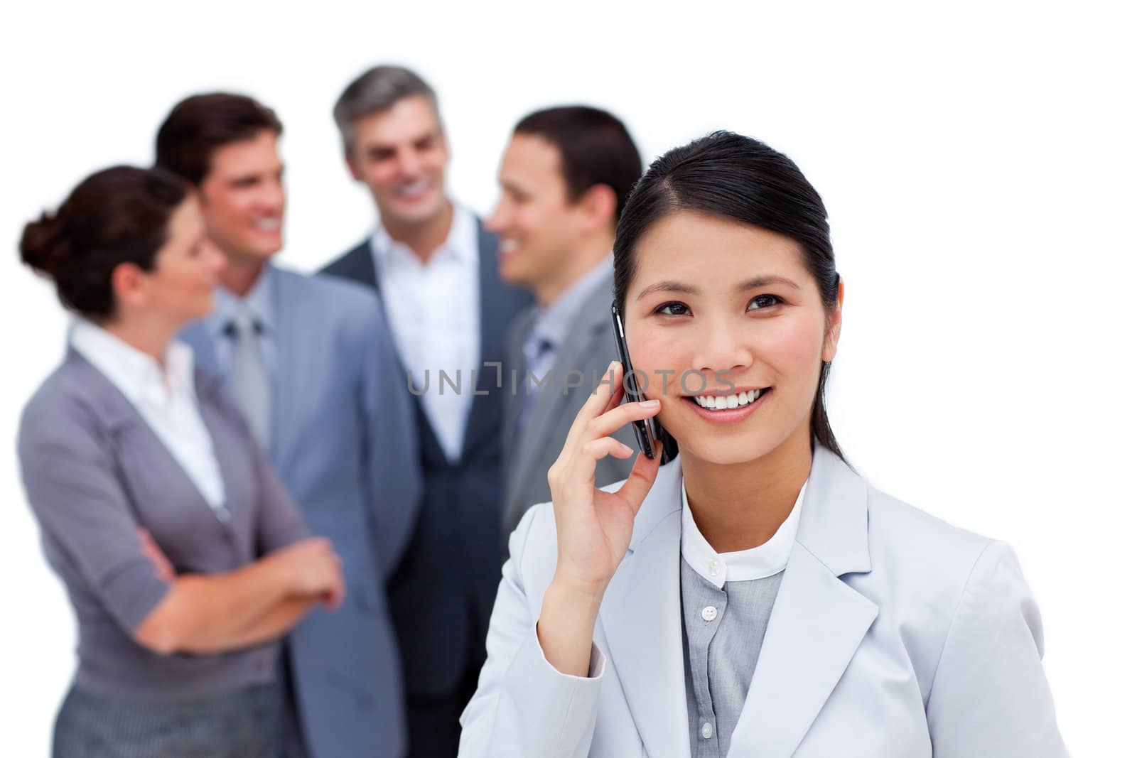 Jolly businesswoman talking on phone in front of her team against a white background