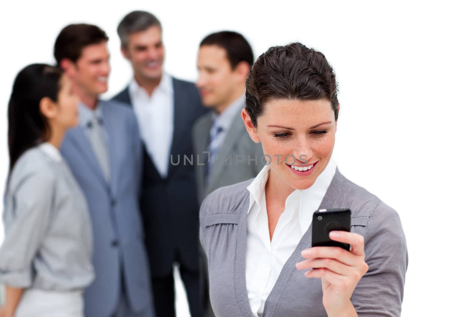 Attractive businesswoman looking at her cellphone in front of her team against a white background
